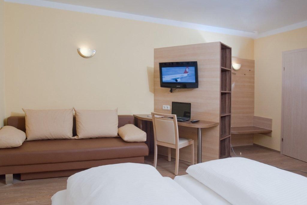 Hotel room with sofa, desk, TV and bed.