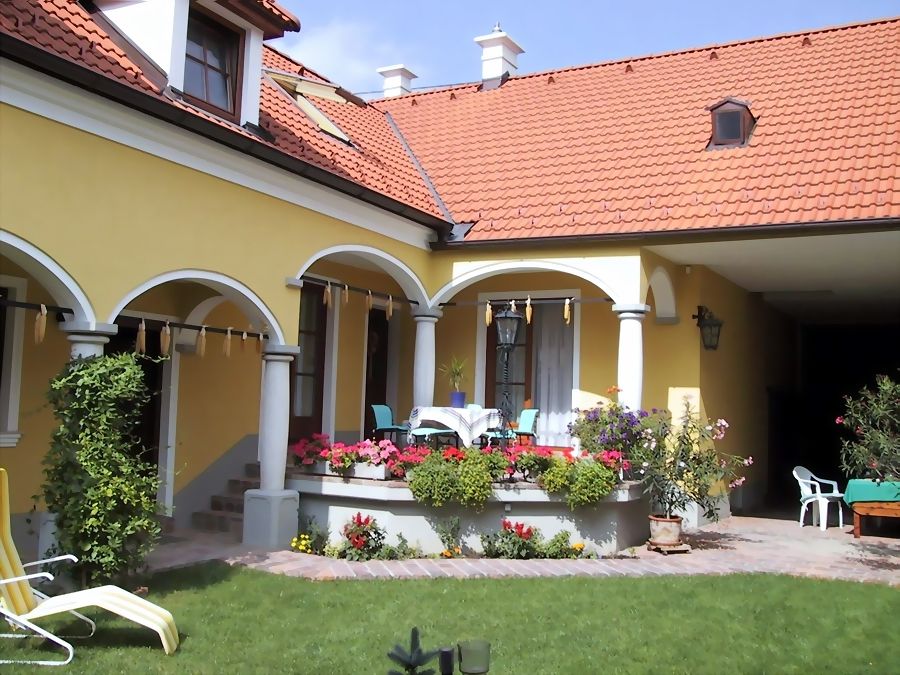 Yellow house with red roof, arcades and terrace with flowers.