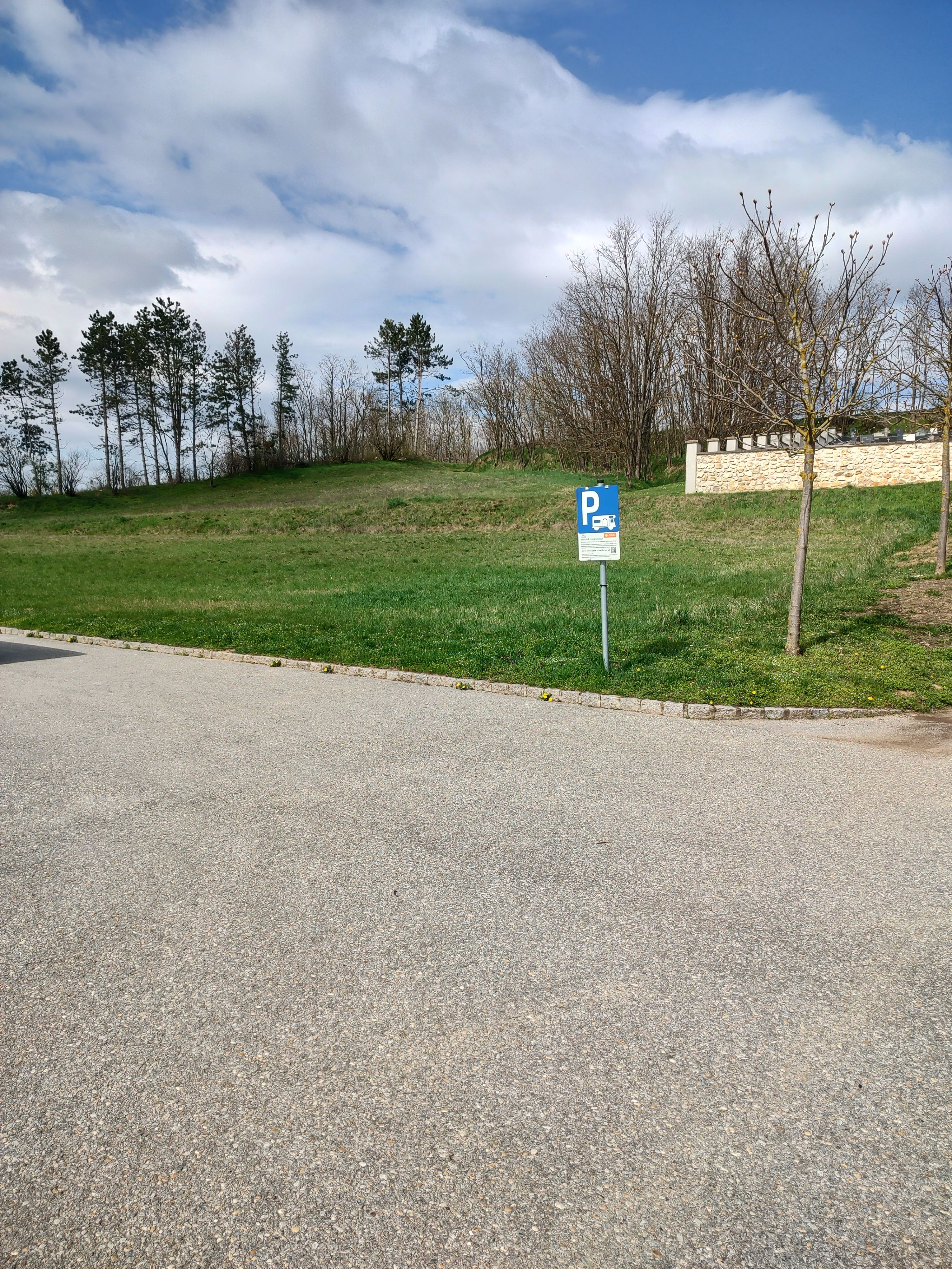 Parking lot sign for motorhomes on an empty parking lot with trees in the background.