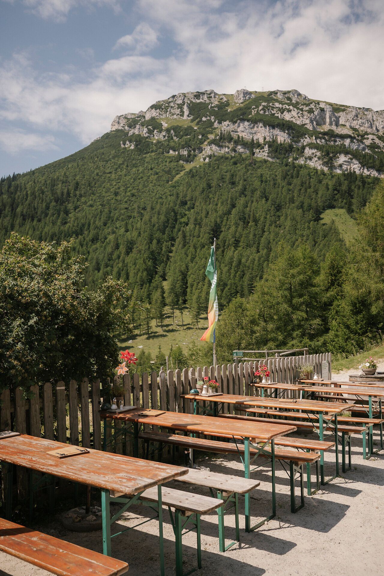 Sunny terrace of the Waxriegelhaus on the Rax, with wooden tables and a view of the surrounding mountain landscape