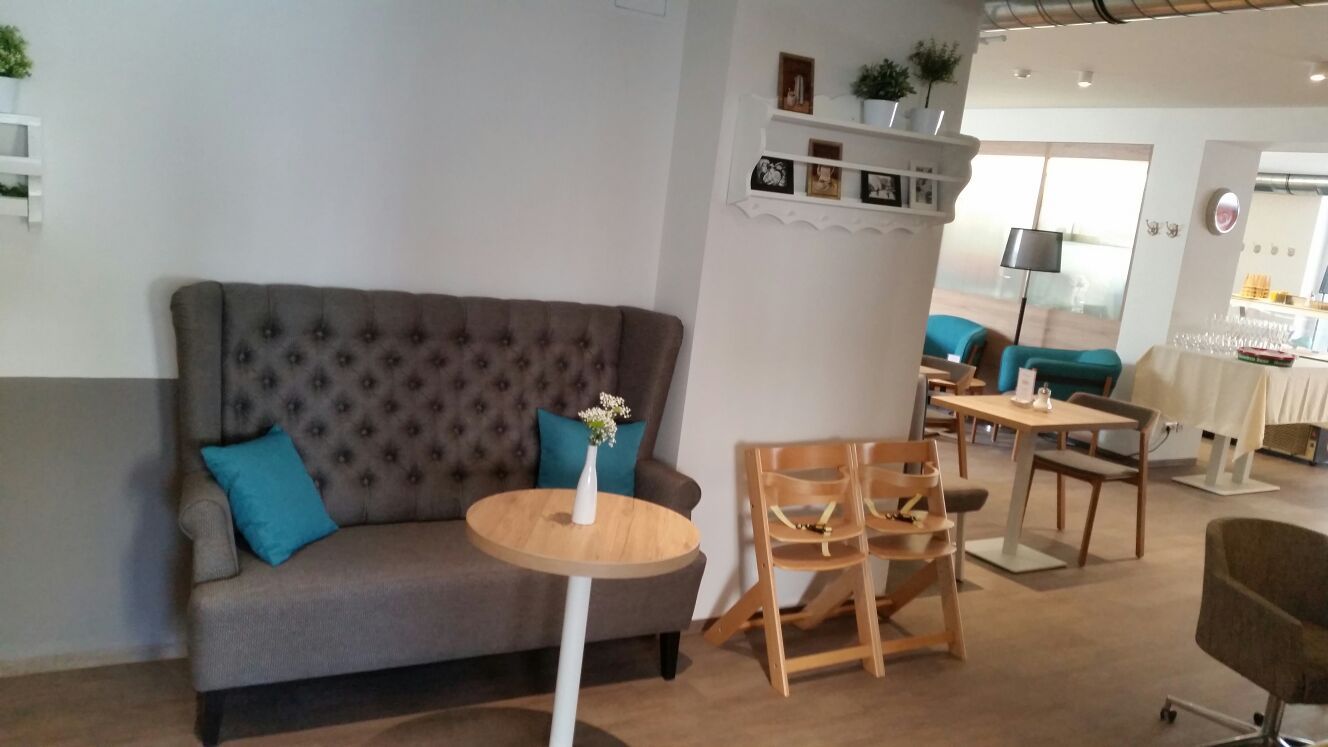 Interior view of a cozy café with a grey sofa, wooden tables and blue cushions.
