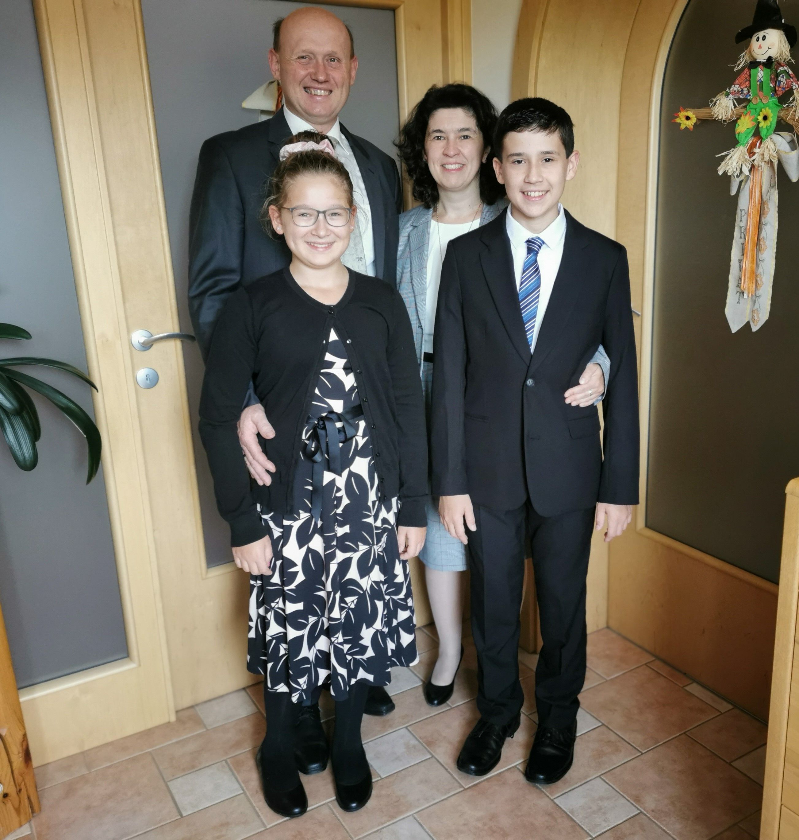 A family in formal dress stands smiling in a hallway.