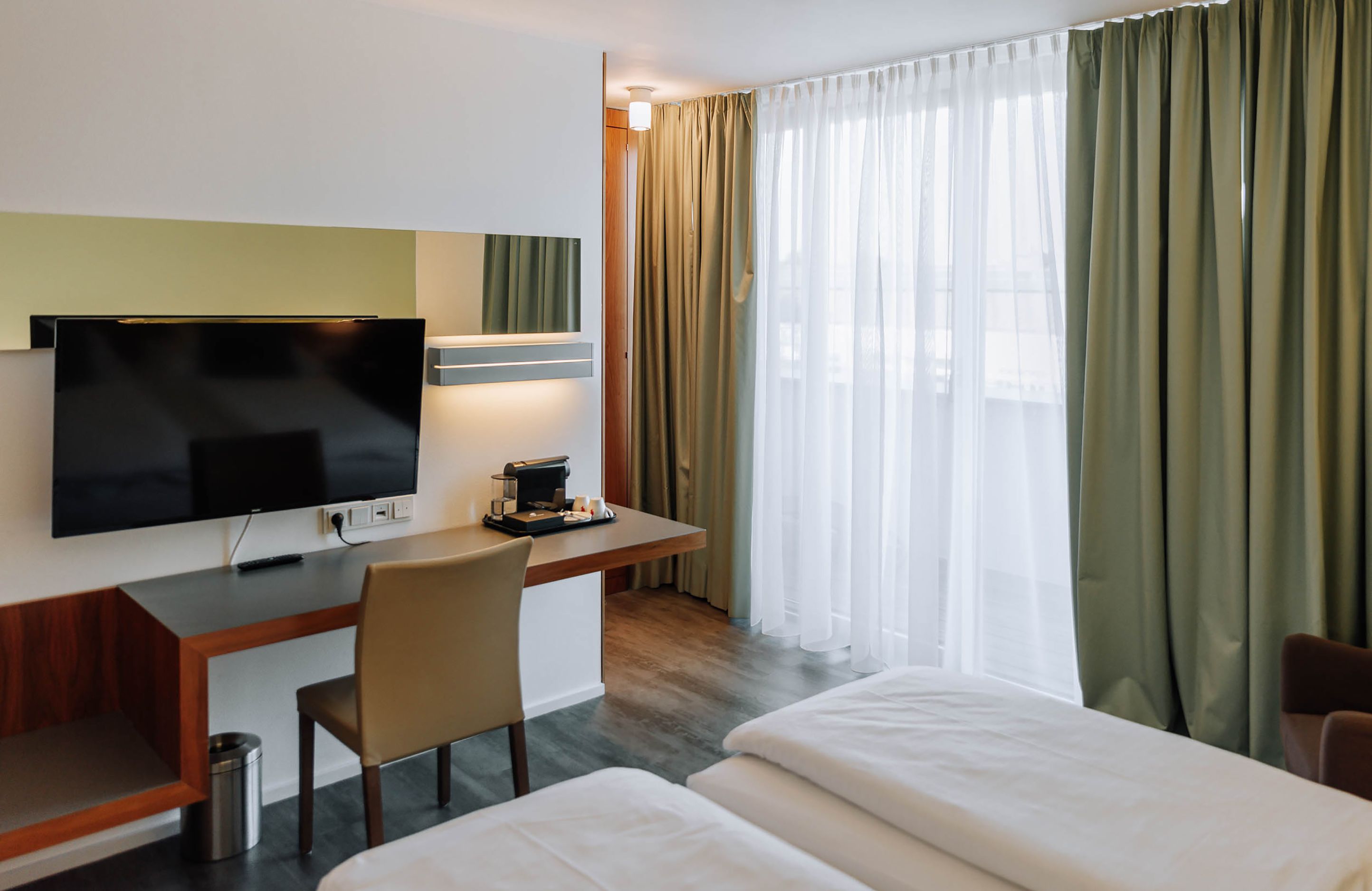 Modern hotel room with desk, TV and curtains.