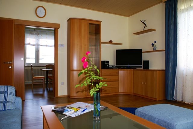 Living room with wooden furniture, TV and vase with flowers.