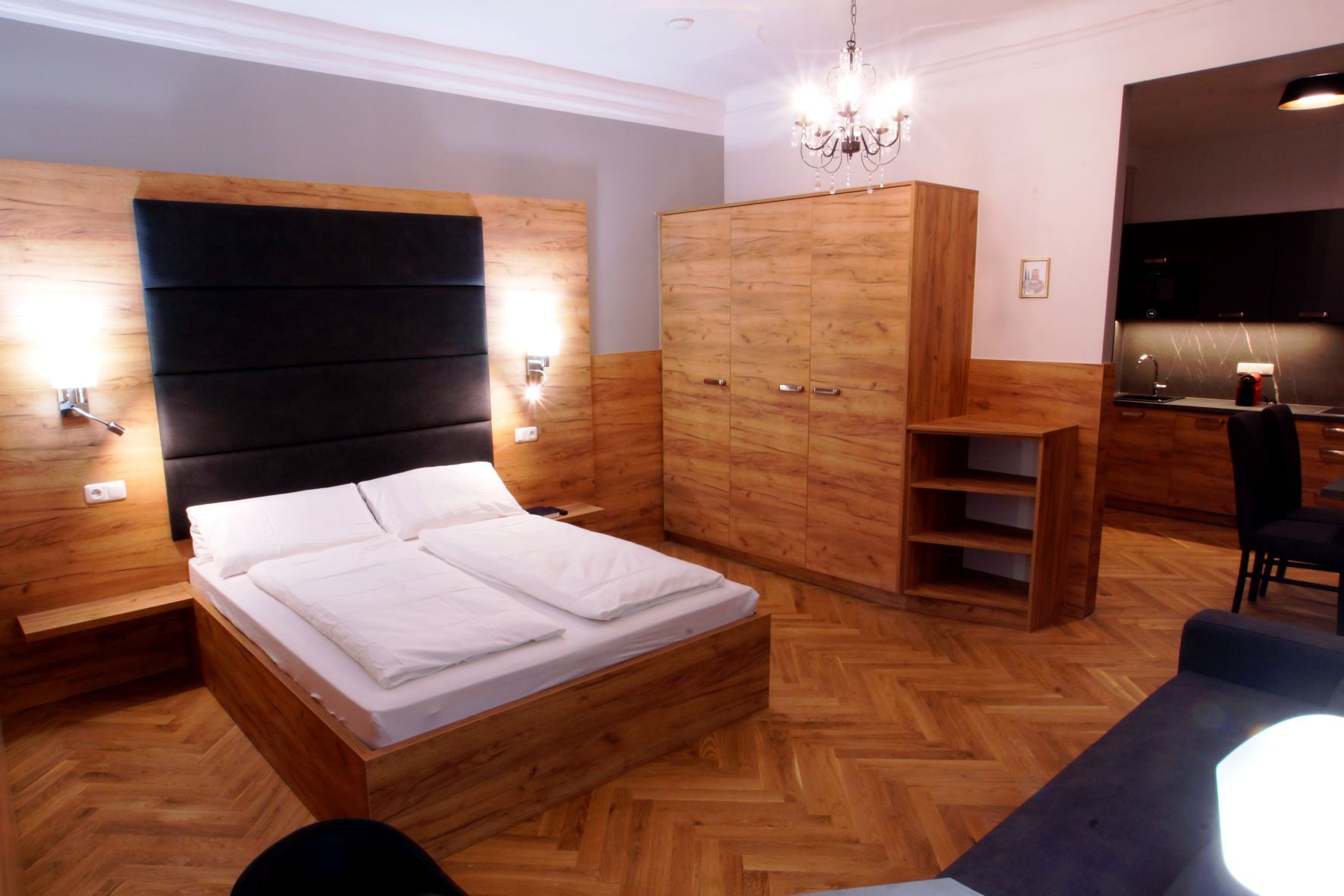 Modern apartment with wooden furniture, double bed, wardrobe, chandelier and kitchenette.