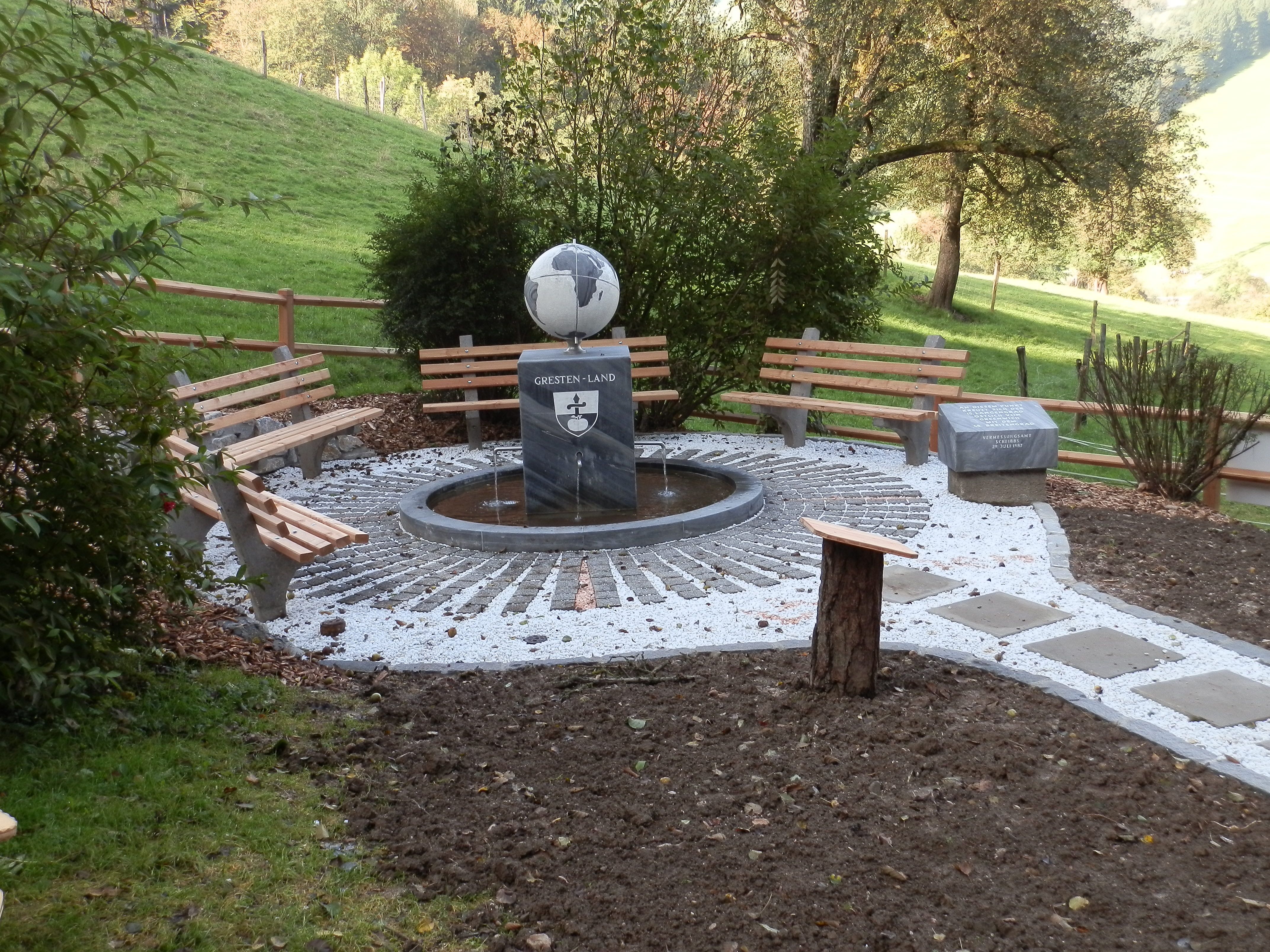 A rest area with benches and a meridian stone in a rural setting.