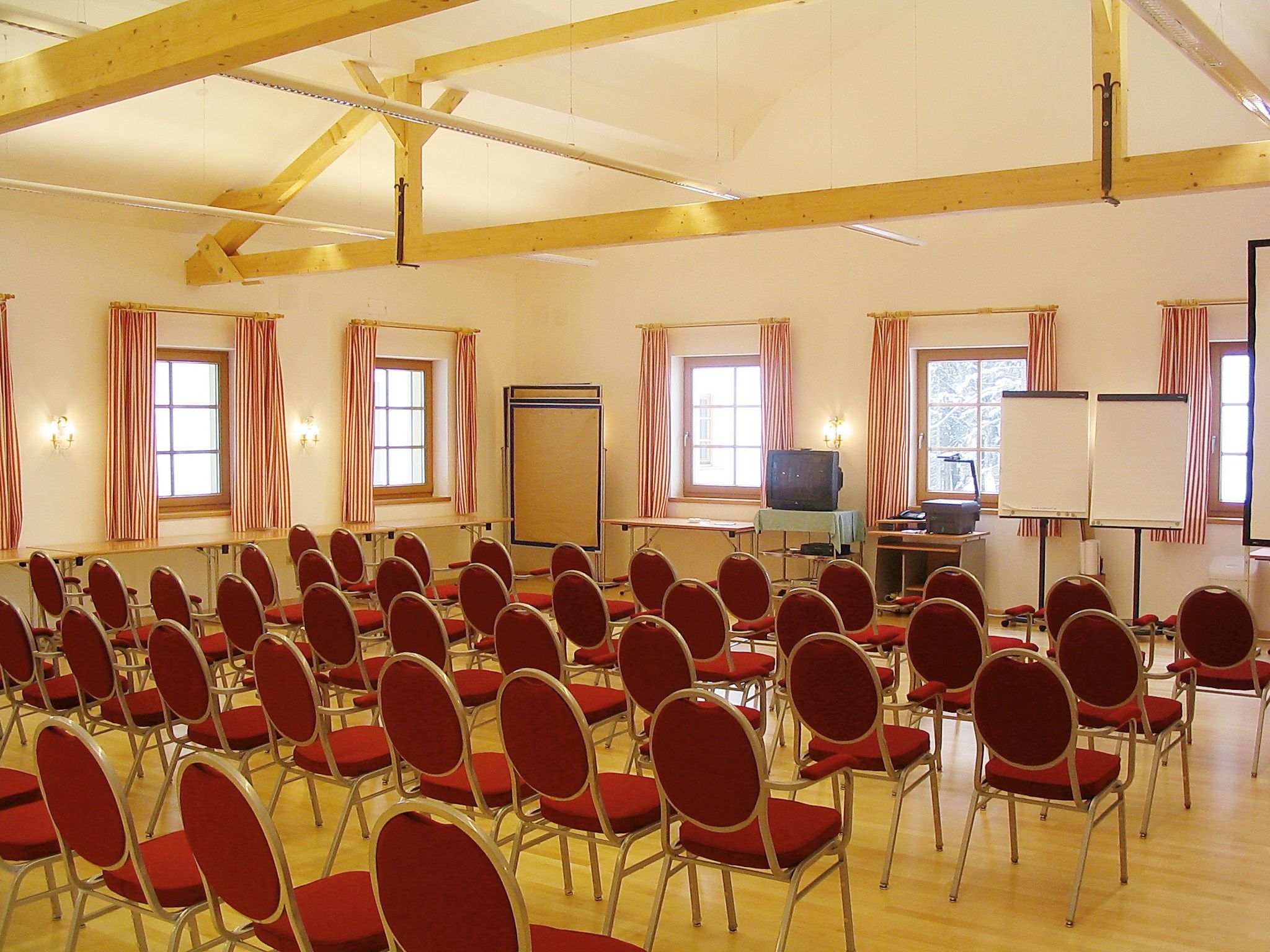 A conference room with red chairs, wooden beams and windows with striped curtains.