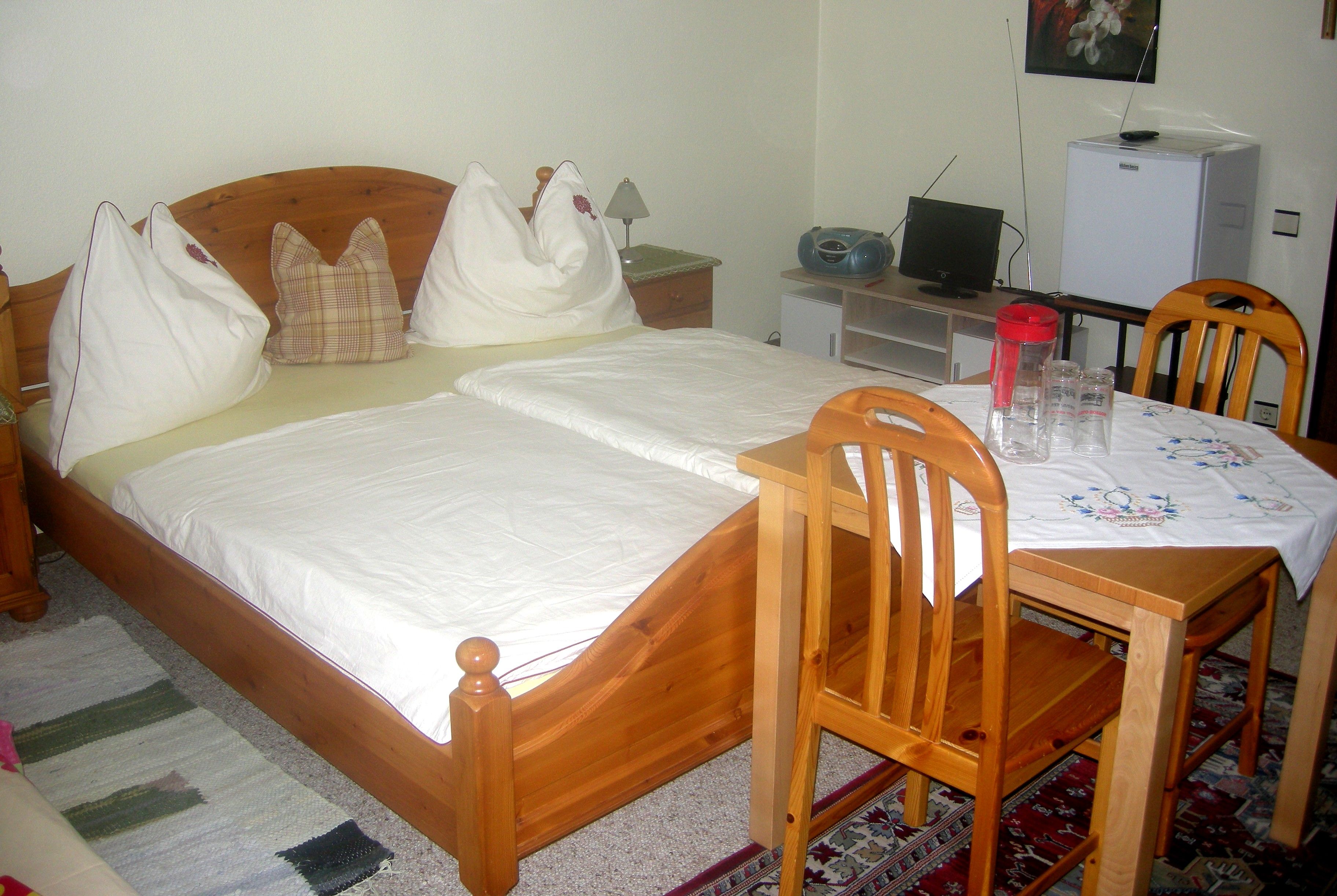 A cozy bedroom with wooden furniture, a double bed, a small table with chairs and a TV.