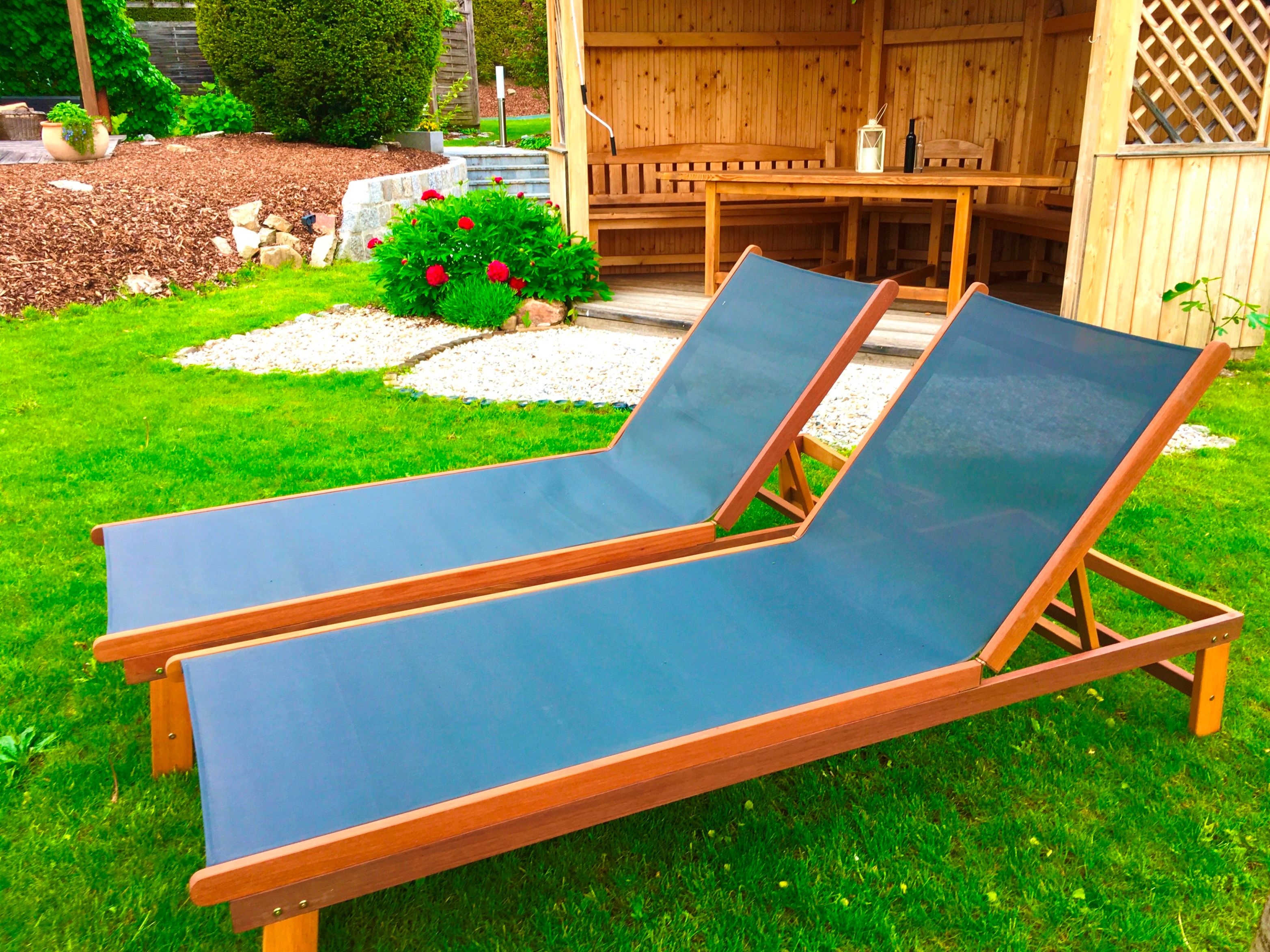 Two blue deckchairs on a green lawn in front of a wooden hut in the garden.