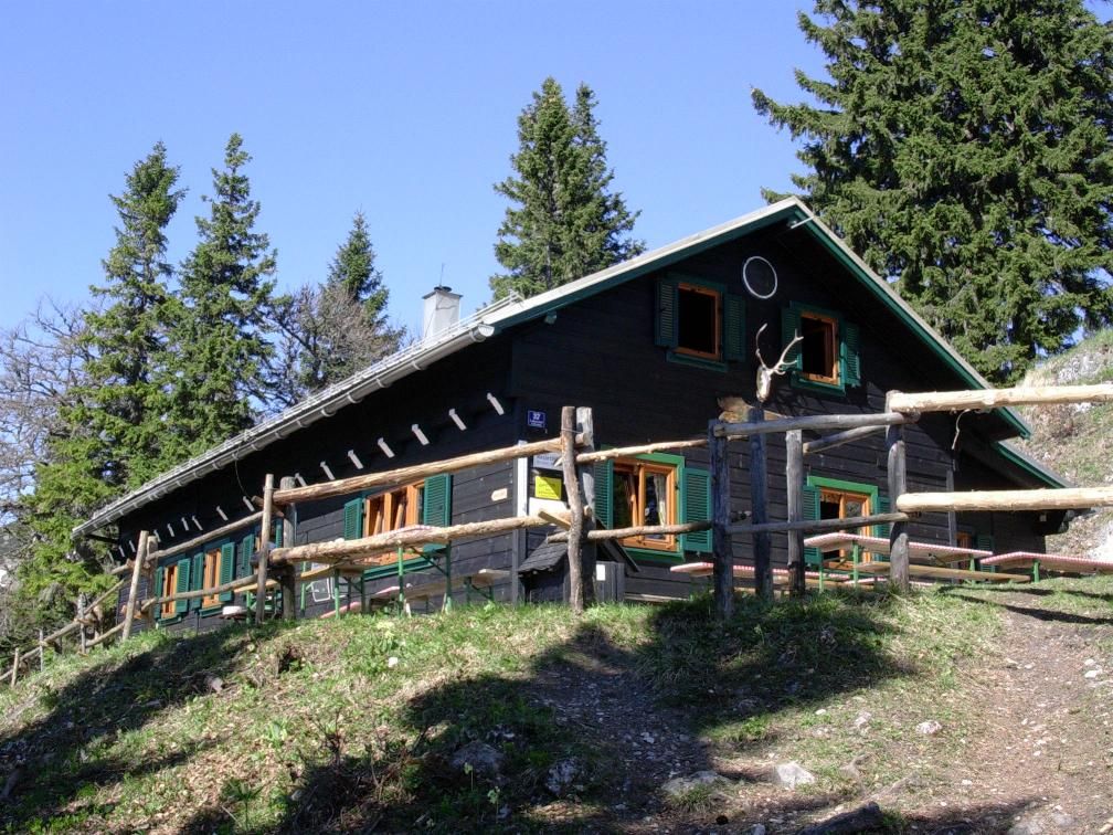 A mountain hut with a wooden fence, surrounded by trees, in sunny weather.