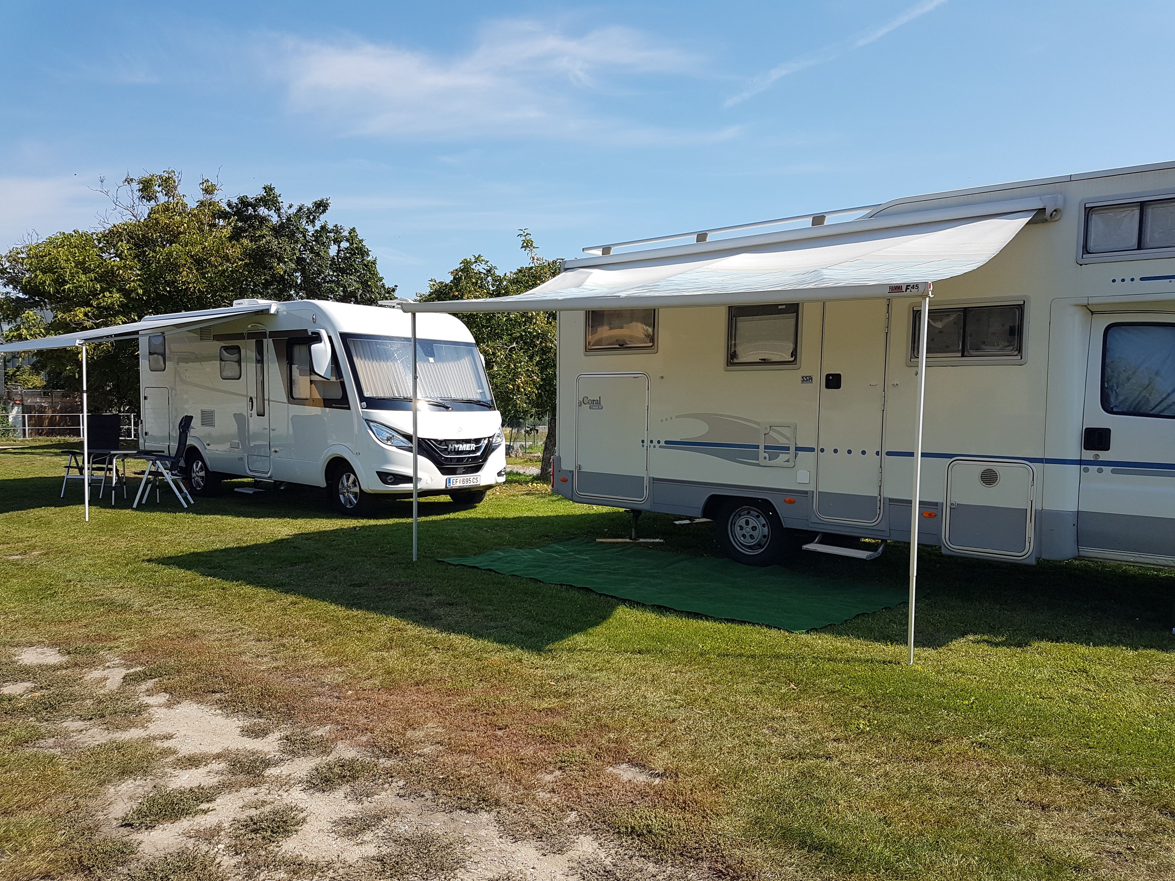 Two motorhomes with extended awnings on a campsite.