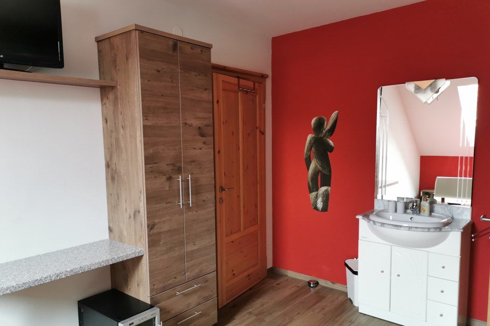 Room with red wall, wooden cupboard, washbasin and mirror.