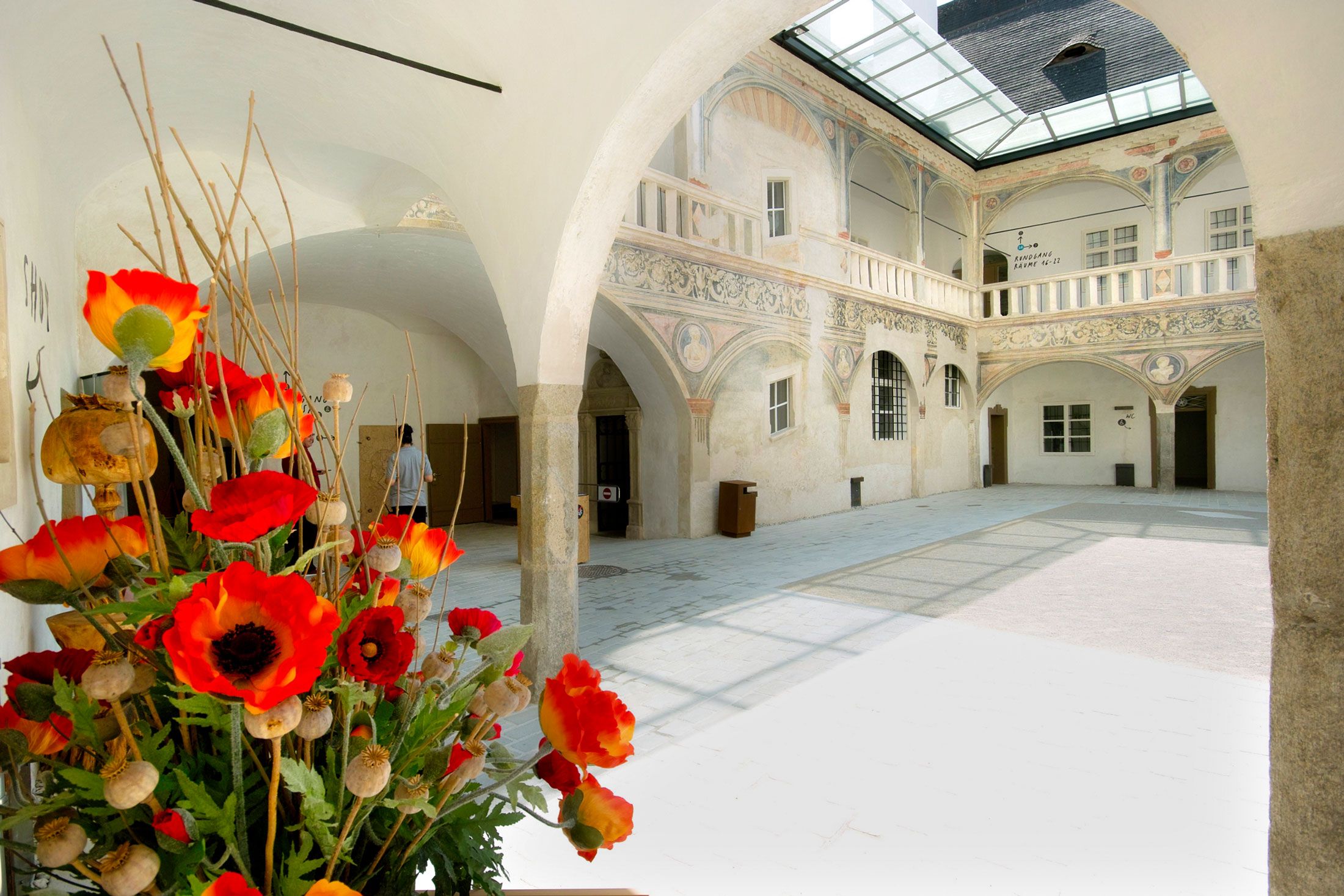 A historic arcaded courtyard with ornate walls and a floral arrangement in the foreground.