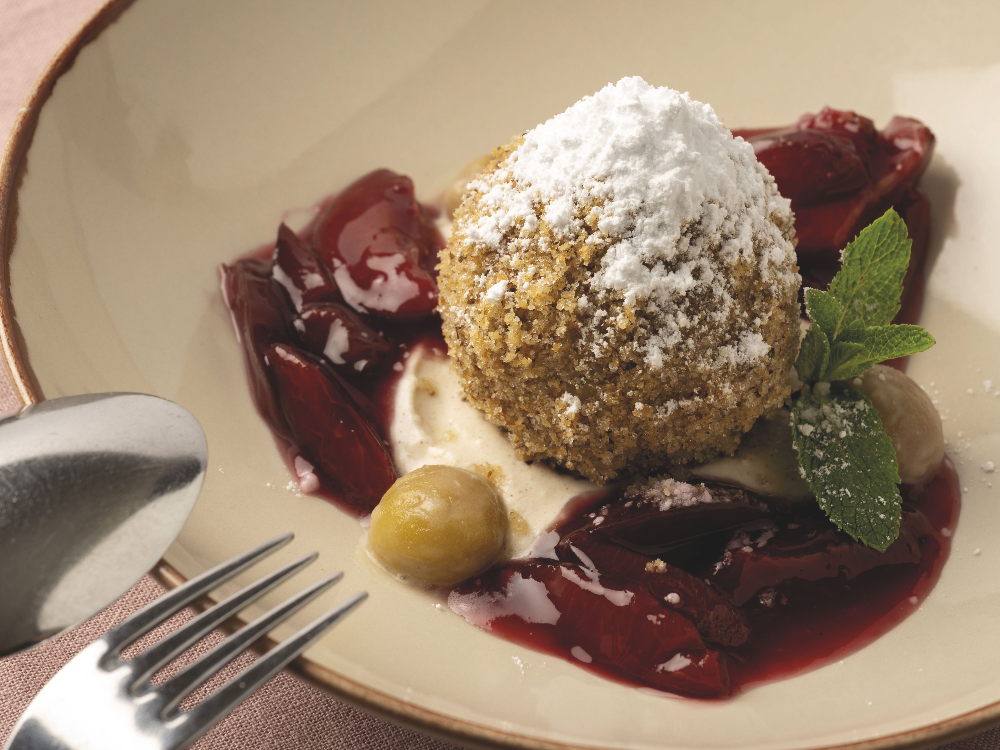 A dessert featuring a dumpling sprinkled with powdered sugar, served on a plate and garnished with red berries and mint leaves.