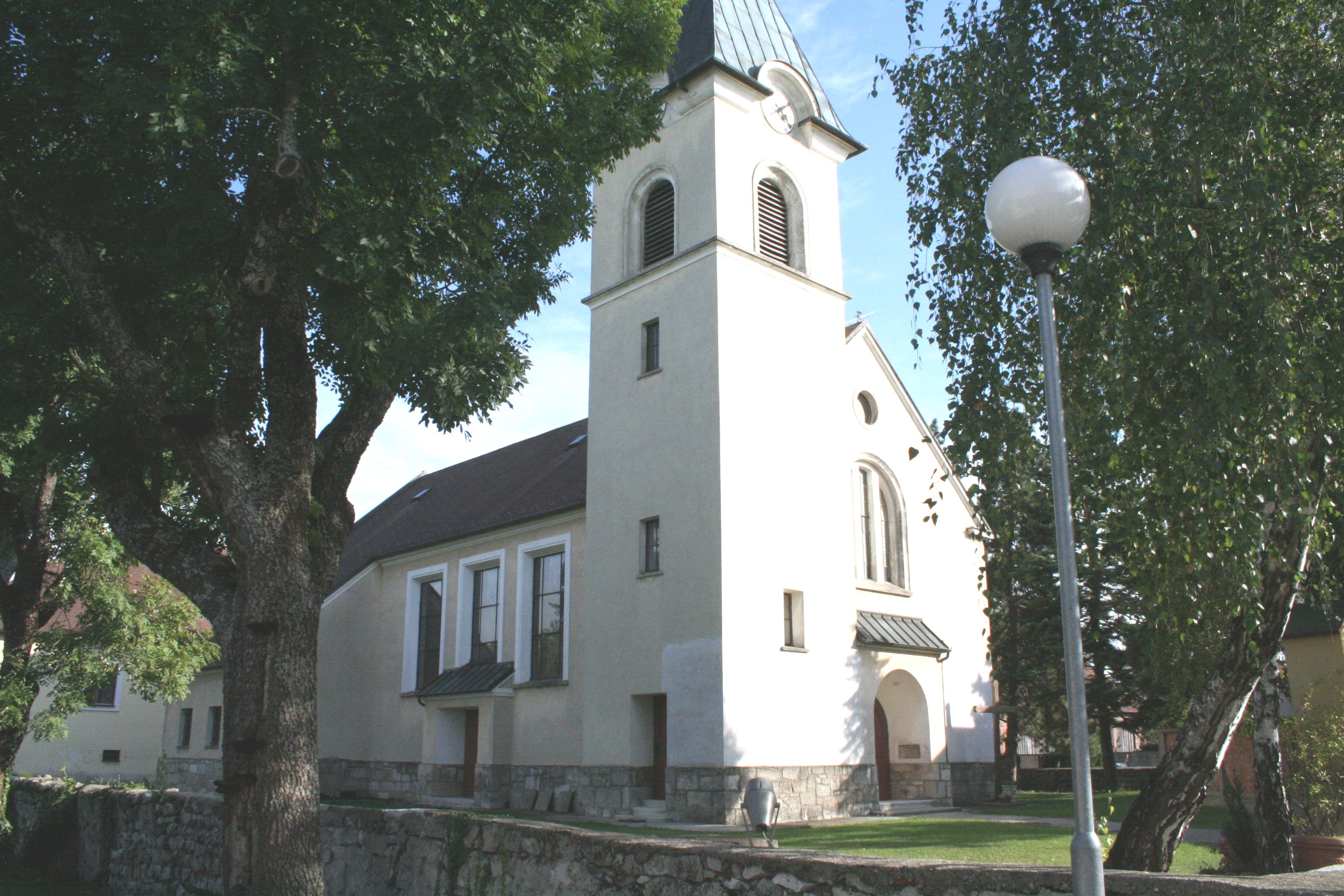 Church in Pischelsdorf with tower and trees in the foreground.