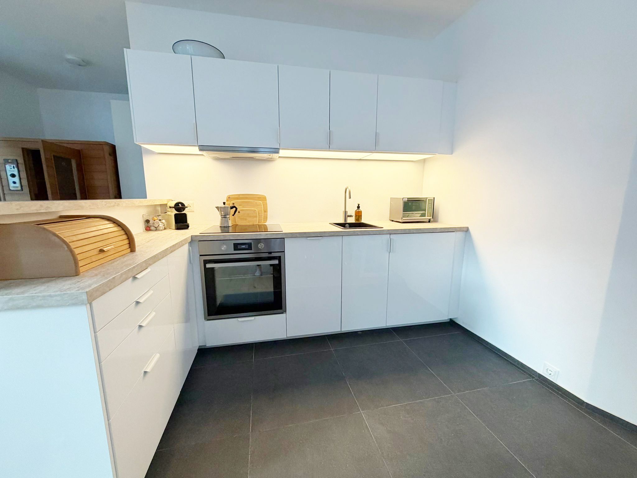Modern kitchen with white cupboards, oven, sink and toaster.