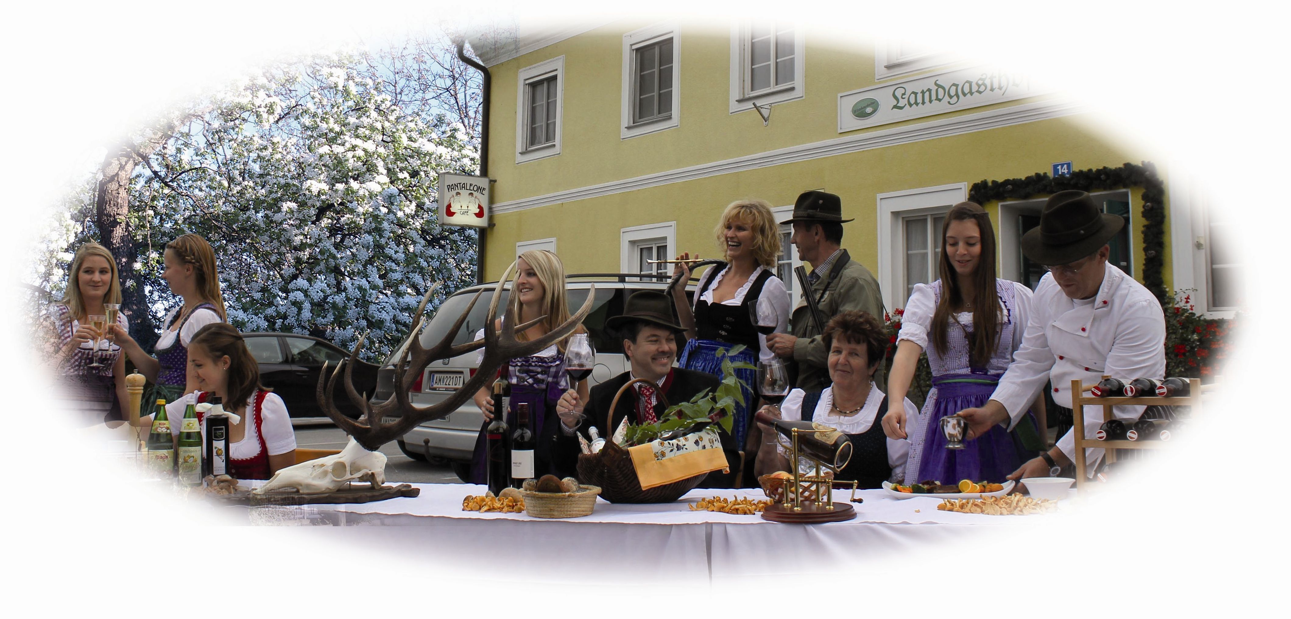 People in traditional costume celebrate in front of a country inn with food and drink.