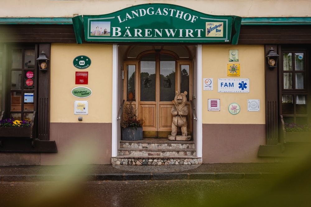 Entrance to the Landgasthof Bärenwirt with wooden figure of a bear and various signs on the wall.
