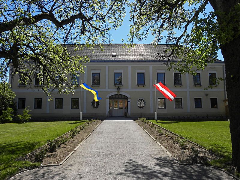 Hochwolkersdorf Castle with two flags, surrounded by trees and lawn.