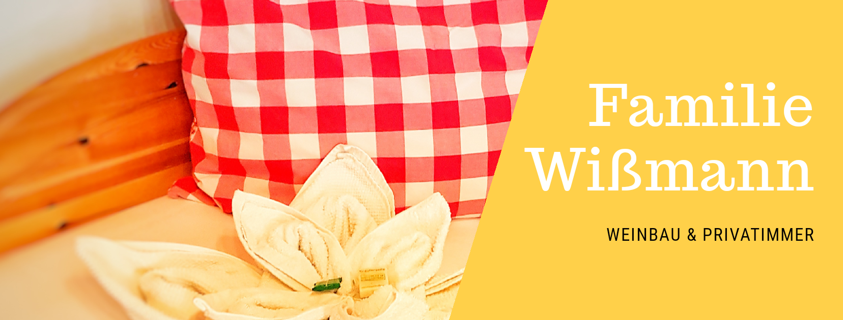 Red cushion with checked pattern and flower-shaped towel on a bed. Text: Wißmann family, winegrowing & private rooms.