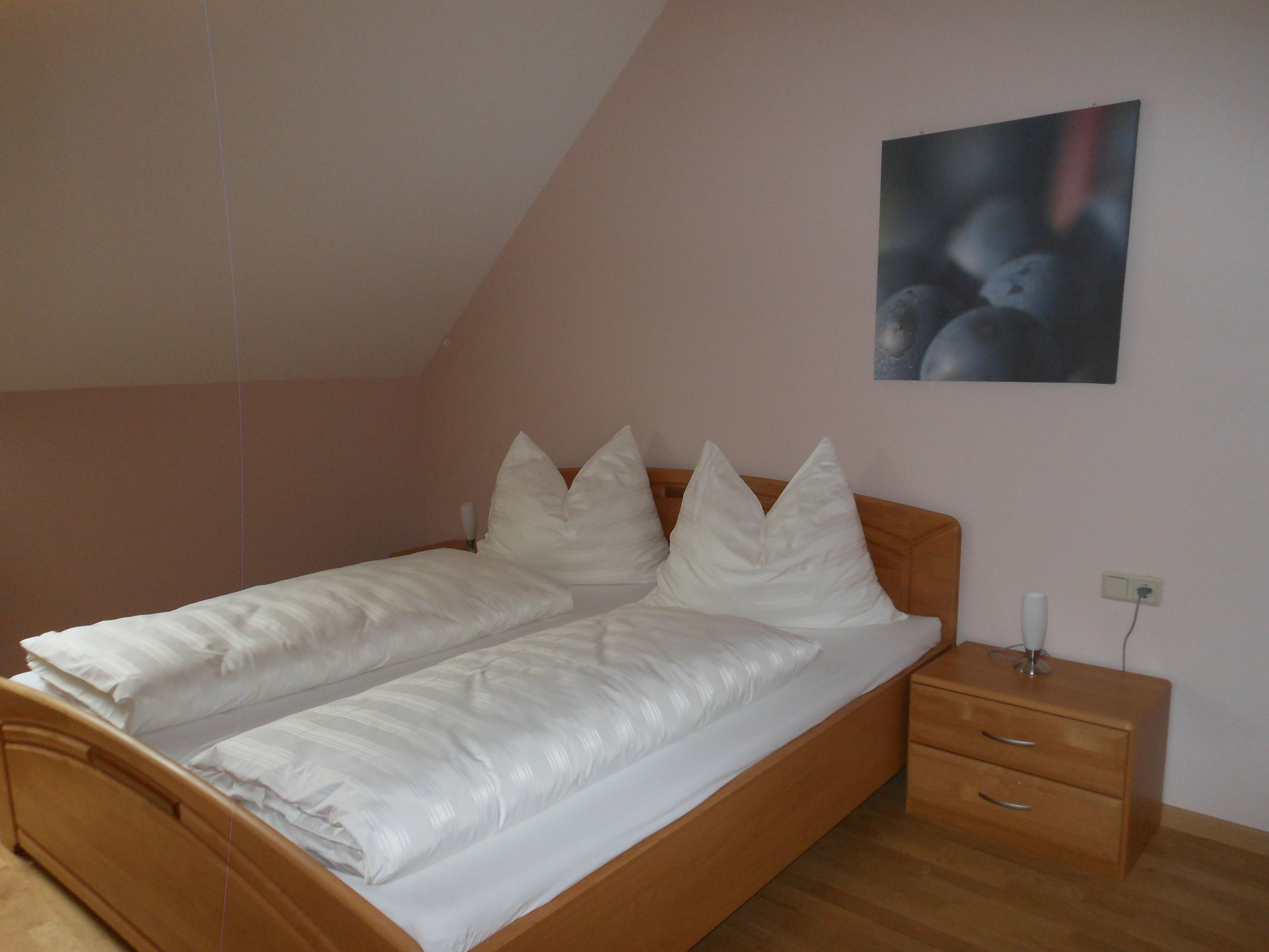 A simple guest room with a double bed, white comforters and a bedside table with lamp.