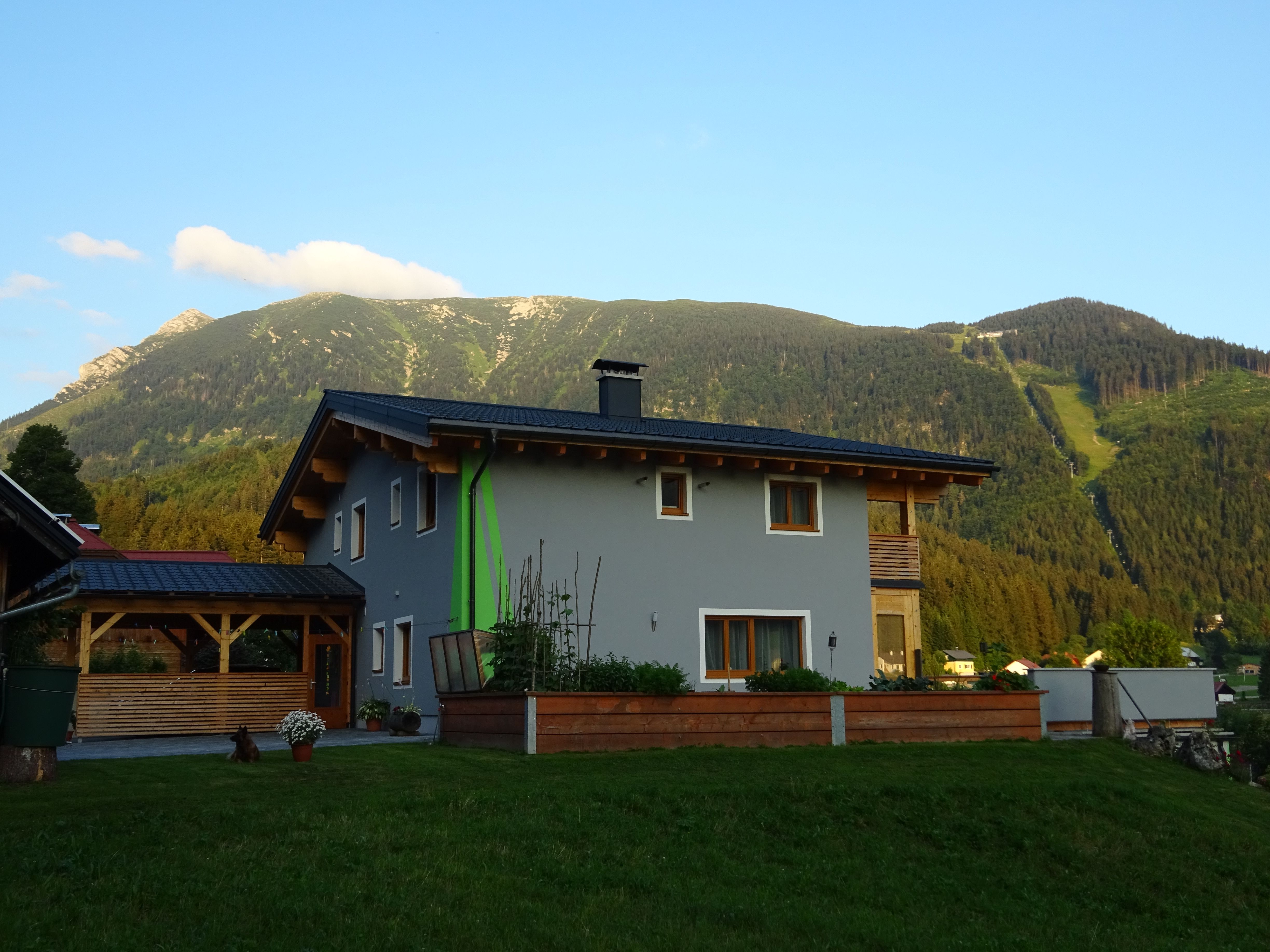 A modern house with a gray façade and wooden elements in front of a mountain landscape.