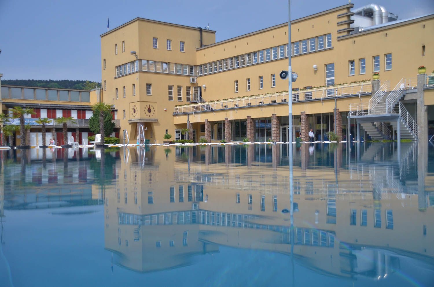 An outdoor pool with a large yellow building in the background, reflected in the water.