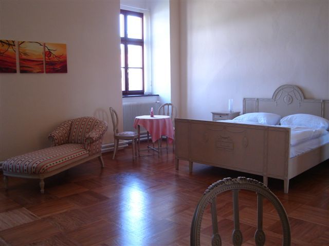 Bright guest room with antique bed, chaise longue and small table.