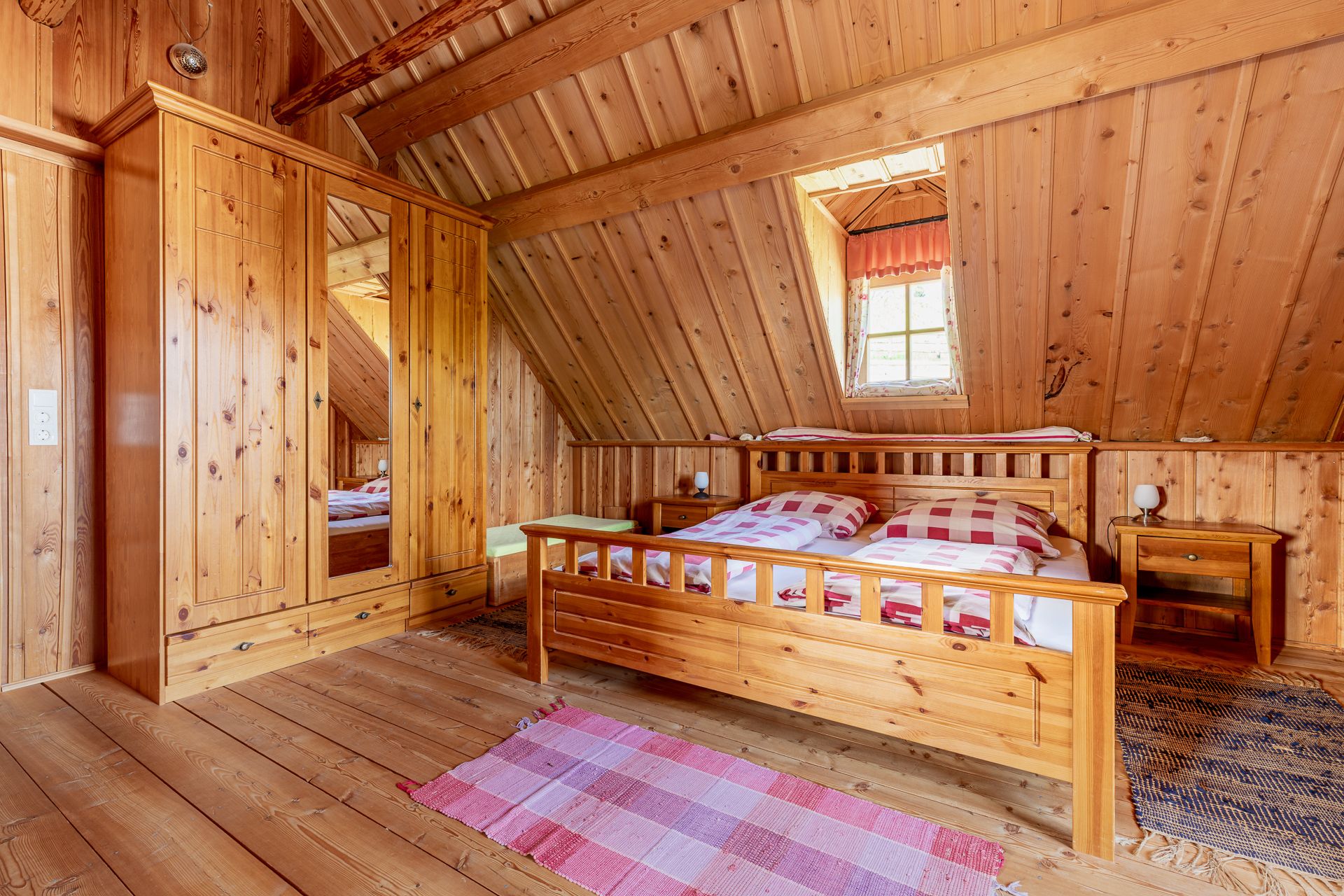 Bedroom with wood paneling, large double bed, wooden wardrobe, carpets and a window.