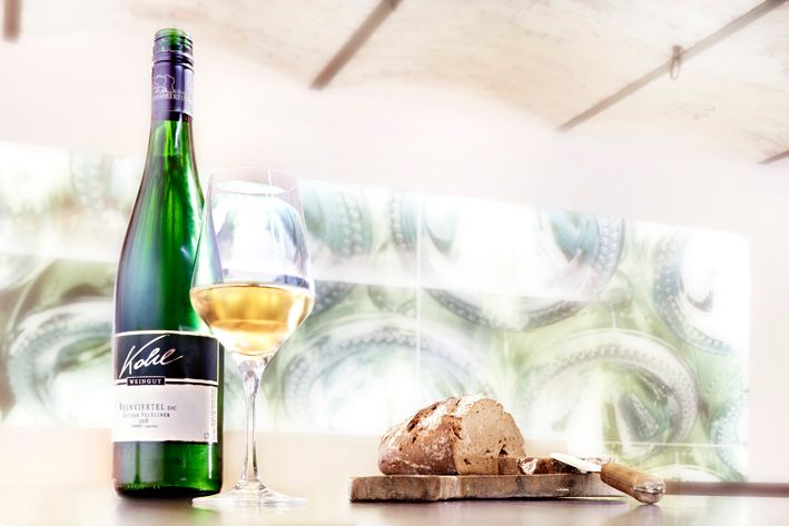 A bottle of white wine, a filled wine glass and a loaf of bread on a table.