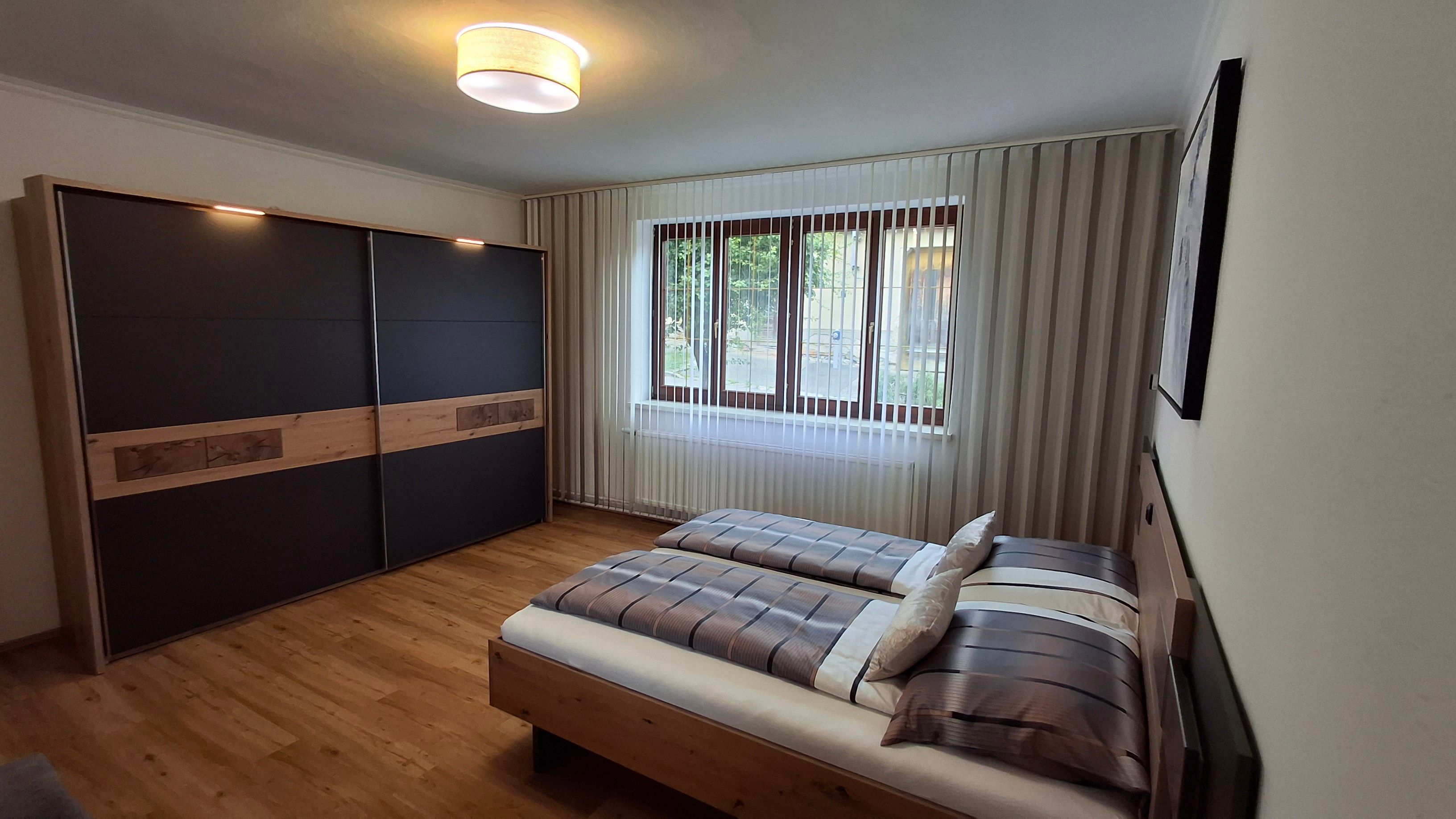 Modern bedroom with double bed, large closet and window with blinds.