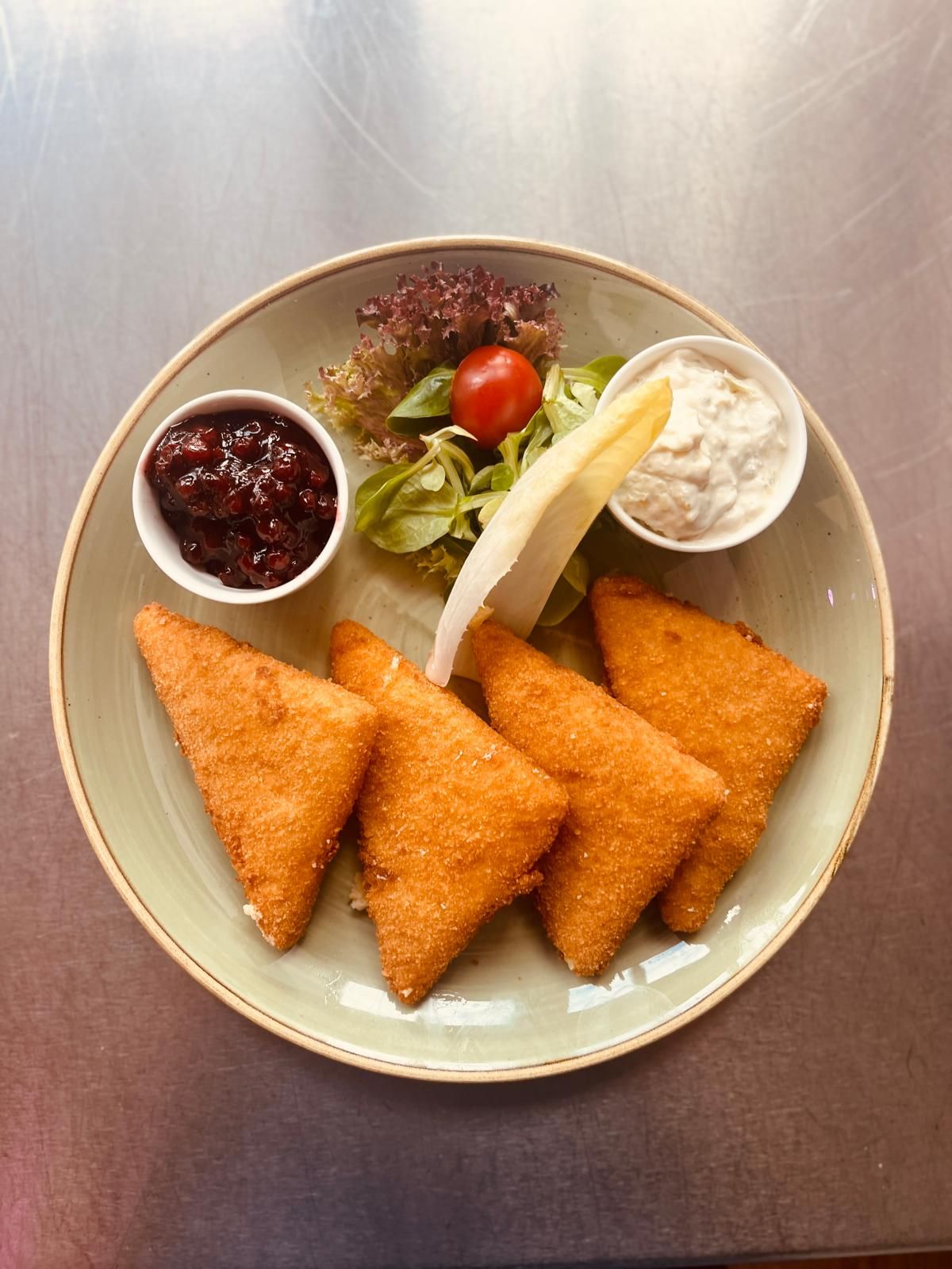 A plate with breaded cheese, salad, cranberries and a white sauce.