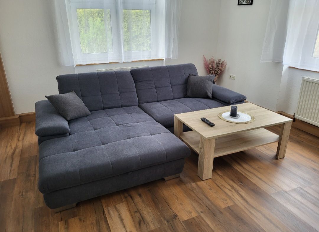 Living room with gray corner sofa and wooden table in front of a window.