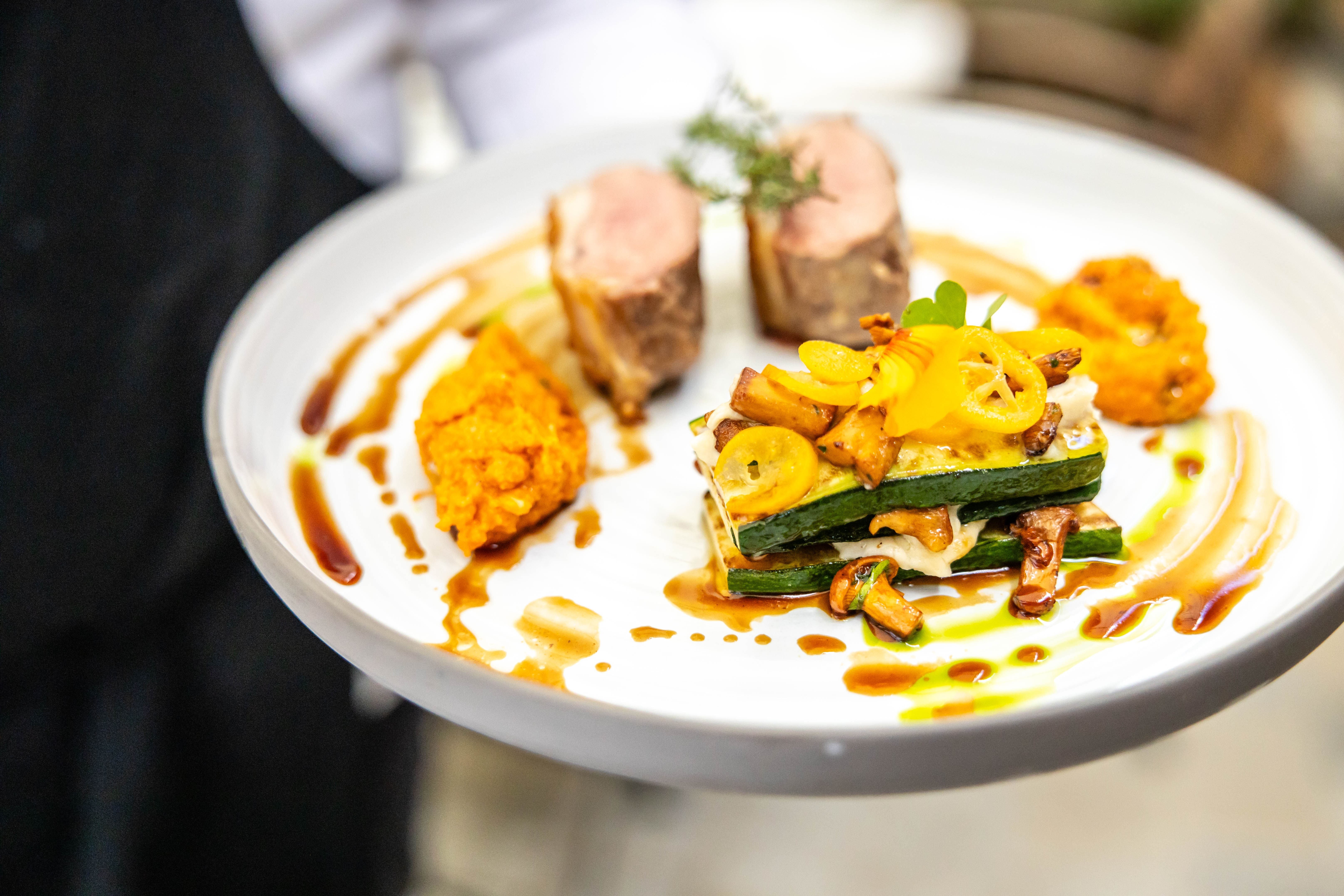 A gourmet dish on a white plate, artfully arranged with meat, vegetables and sauce.