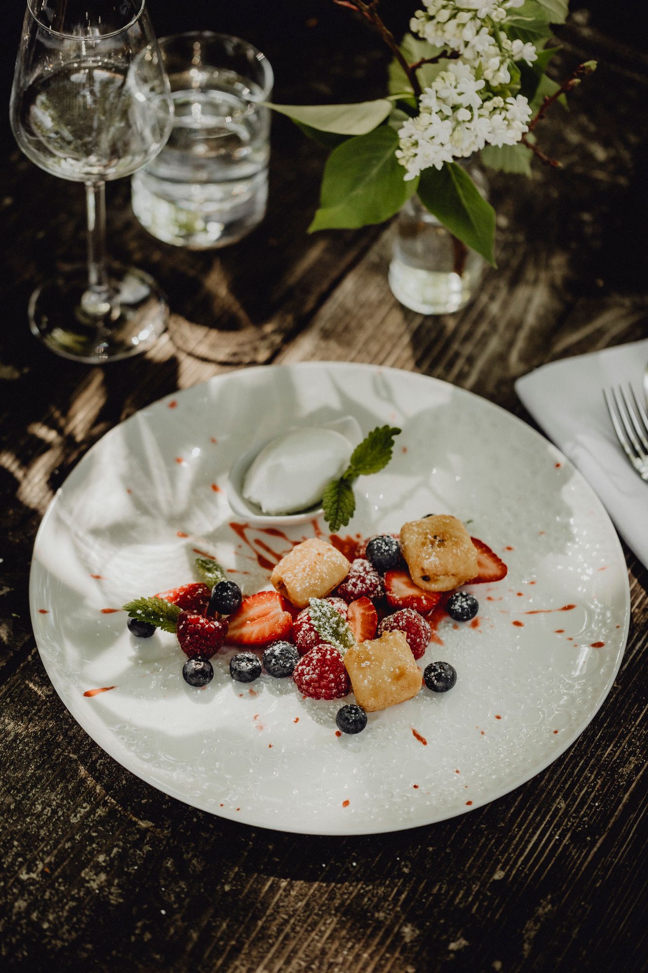 A dessert plate with baked curd cheese, marinated berries and yoghurt ice cream, decorated with mint leaves, on a wooden table.