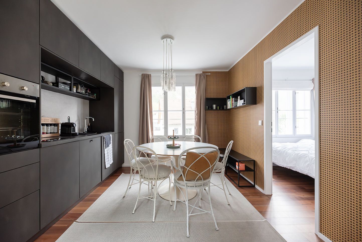 Modern kitchen with dining table and chairs, dark cupboards and wooden floor.