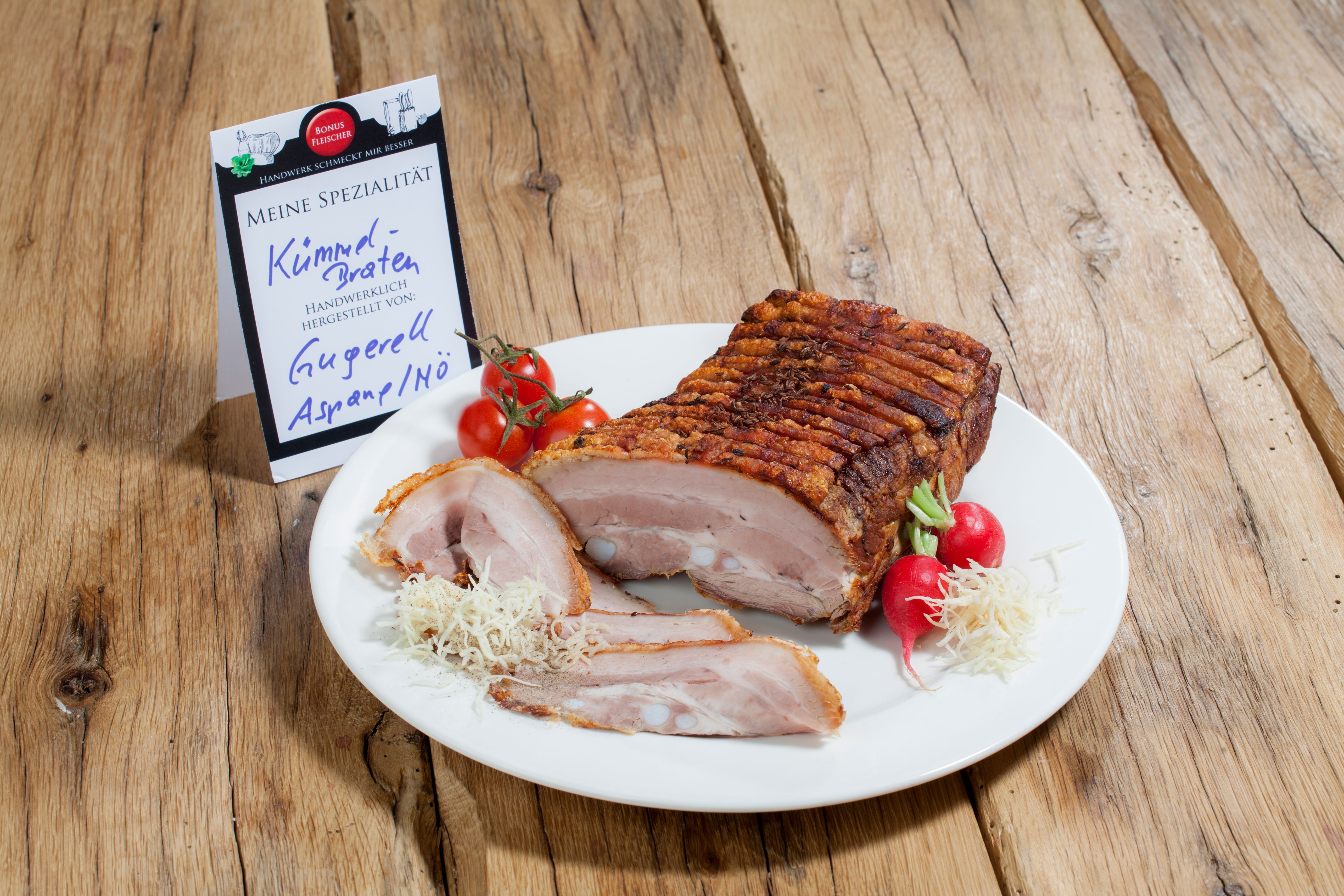 A plate of caraway roast, radishes and tomatoes on a wooden table.