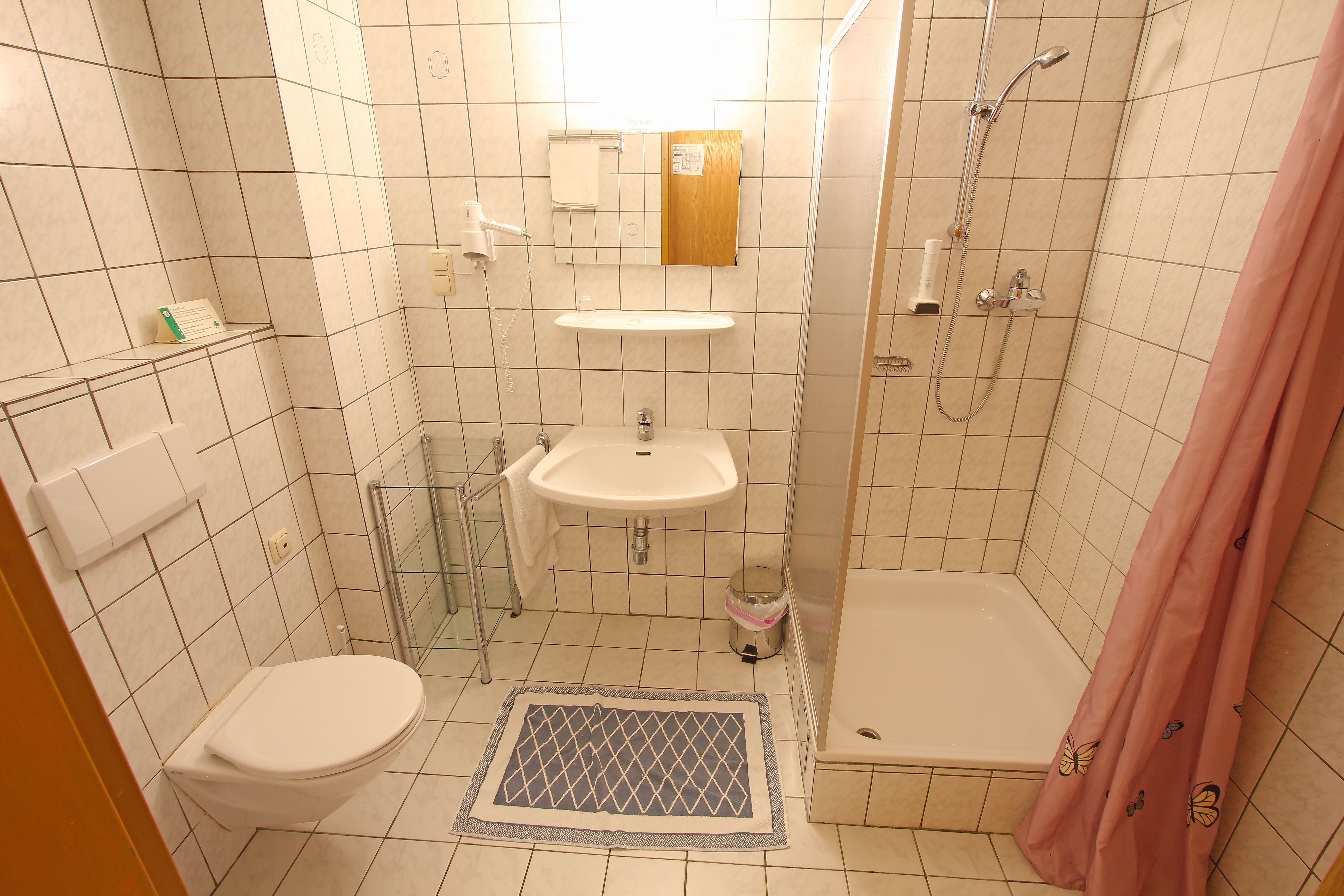 Small bathroom with shower, washbasin and toilet, tiled in white.
