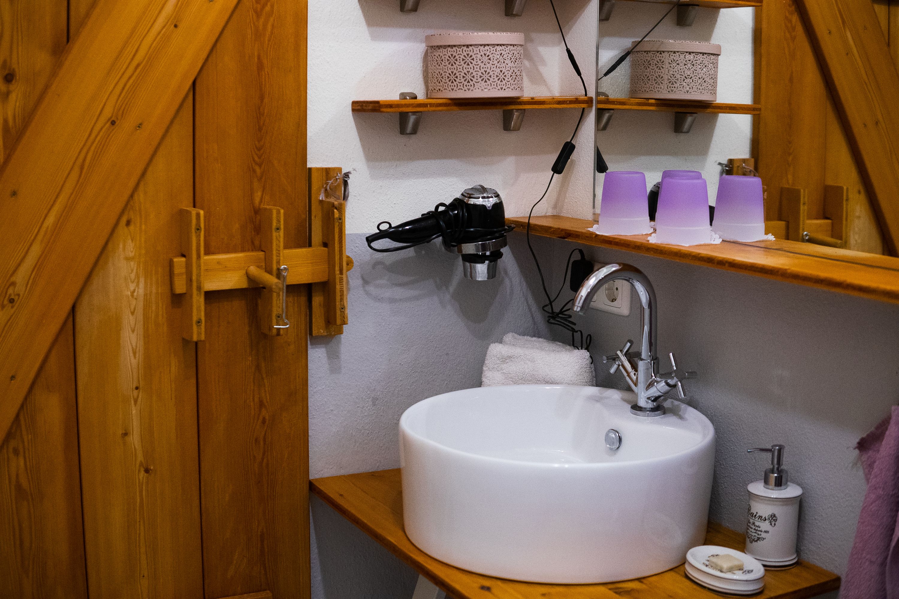 Bathroom with washbasin, mirror, hairdryer and wooden shelves.