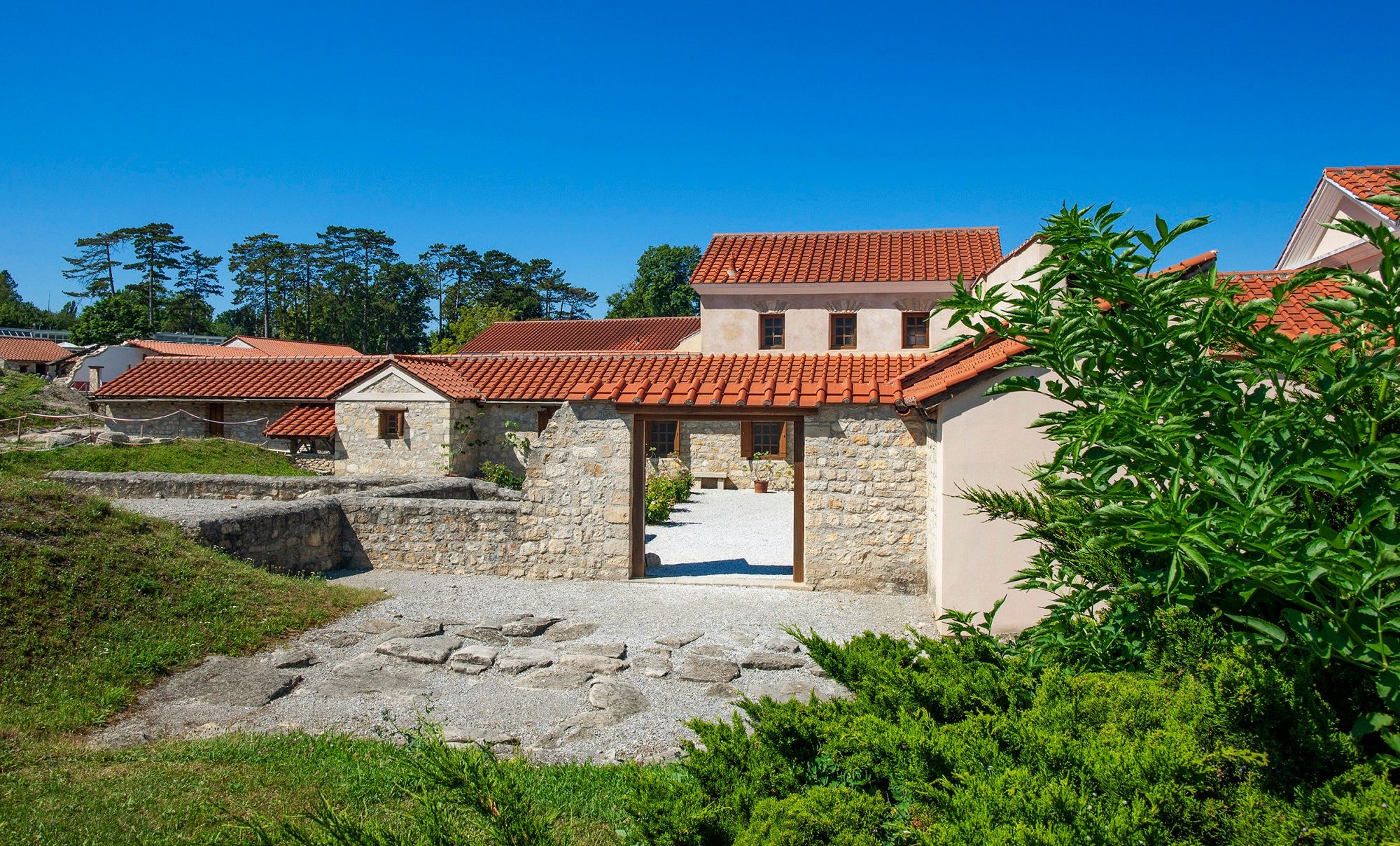 Reconstructed Roman buildings in Carnuntum with red tiled roofs and stone walls, surrounded by green vegetation.