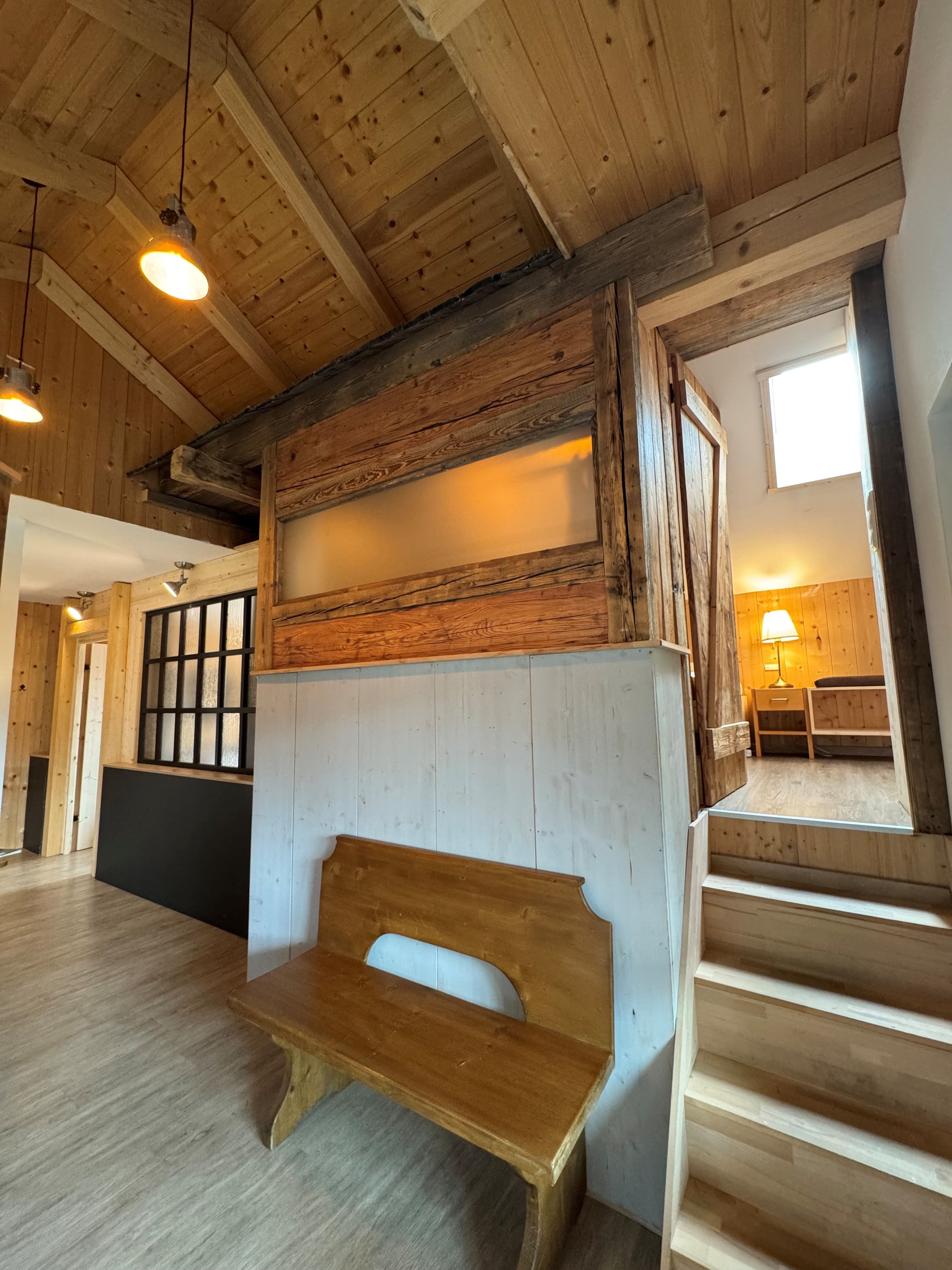 A family room with wooden walls, a wooden floor, and a wooden bench. A staircase leads to a room on a higher level.
