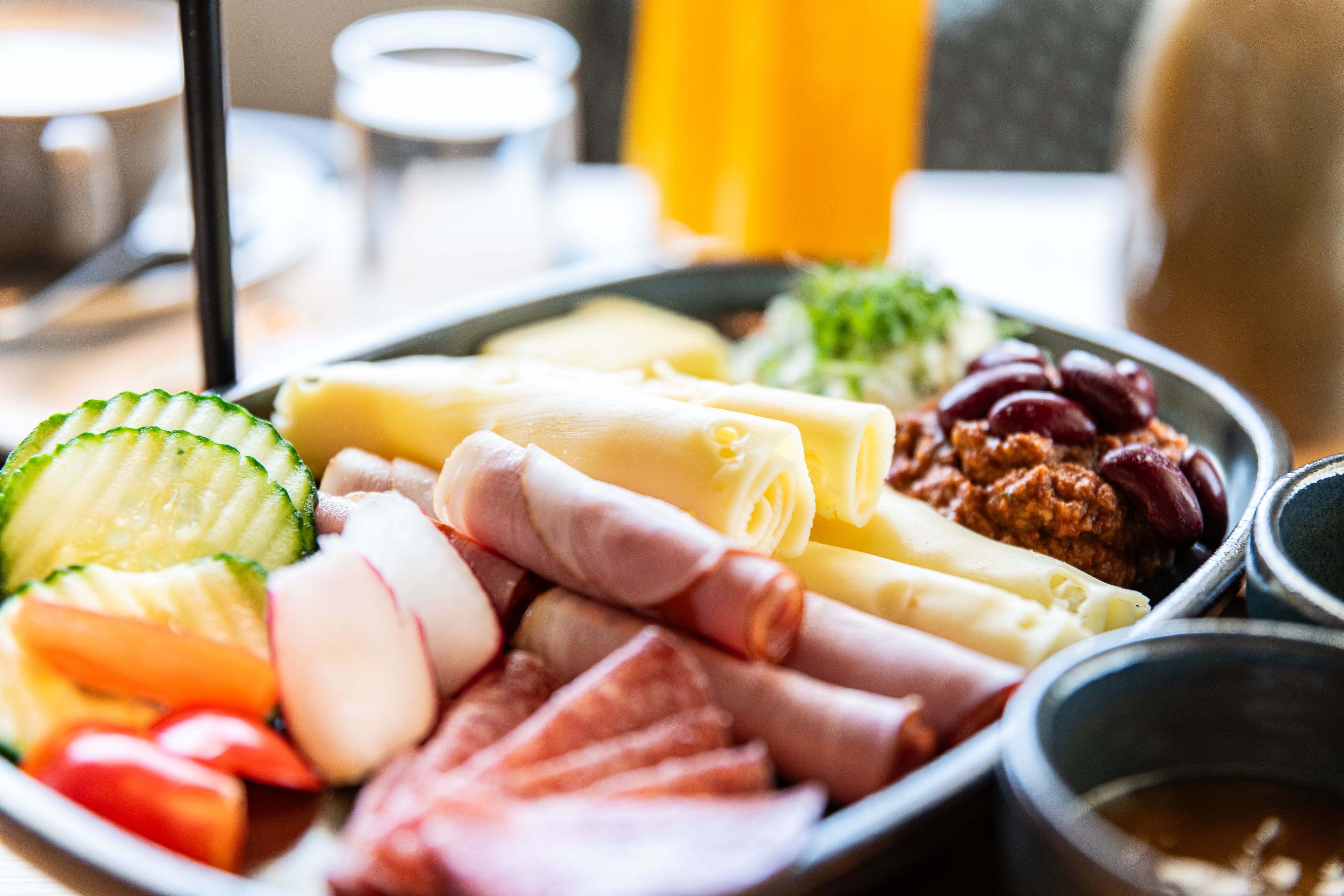 Close-up of a breakfast plate with cheese, ham, salami, vegetables and beans.