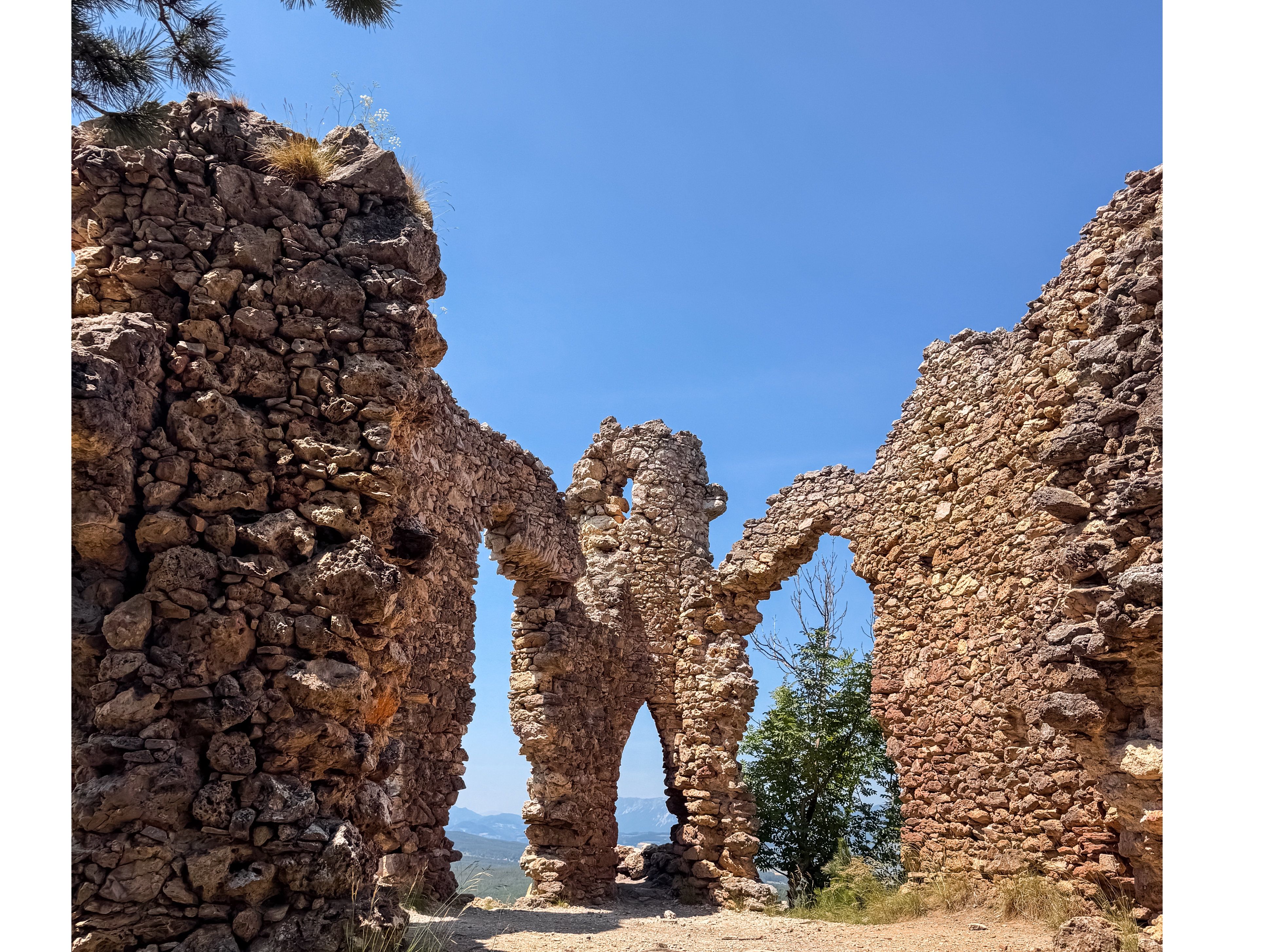 Ruins of an old stone wall with arches under a blue sky.