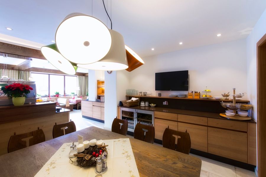 A modern restaurant with wooden furniture, a large table, decorative lamps and a TV on the wall.