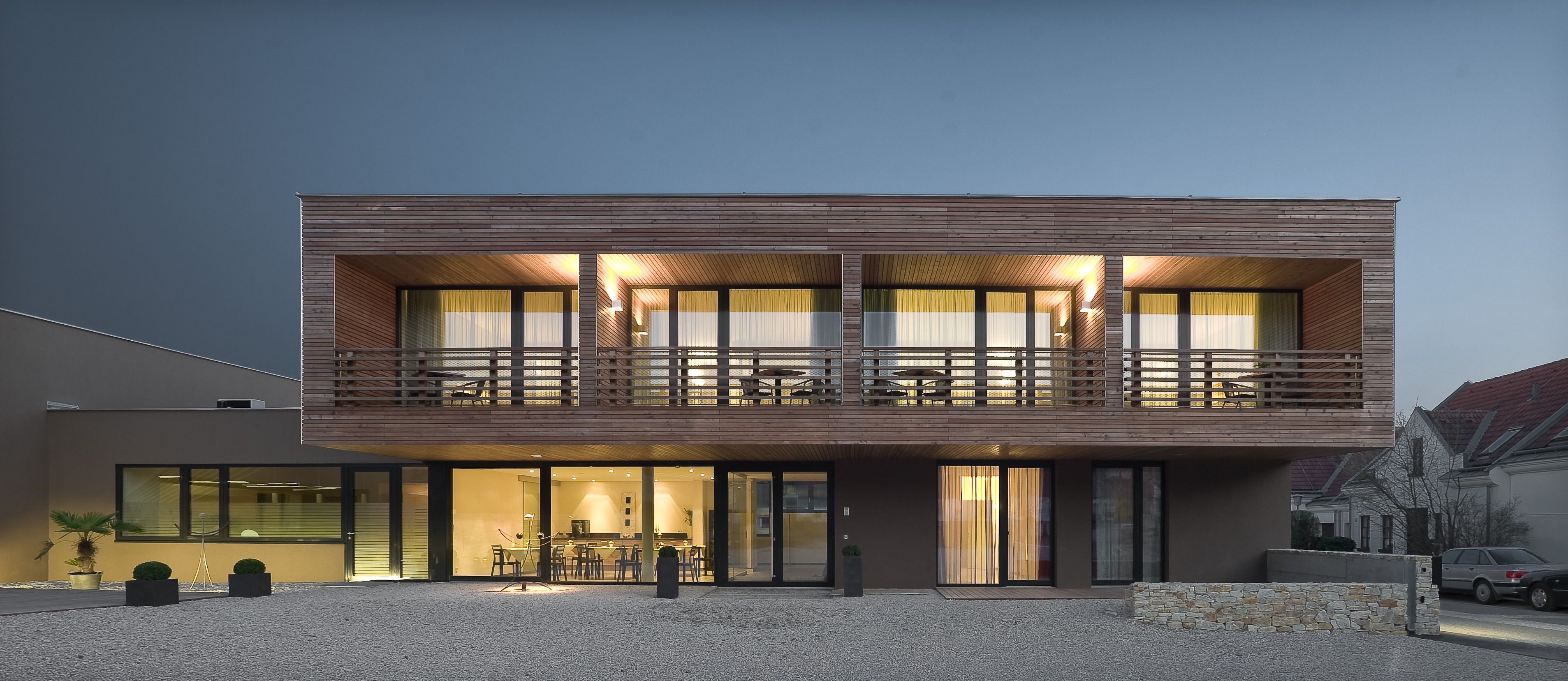 Modern two-story house with wood paneling and large windows with night lighting.