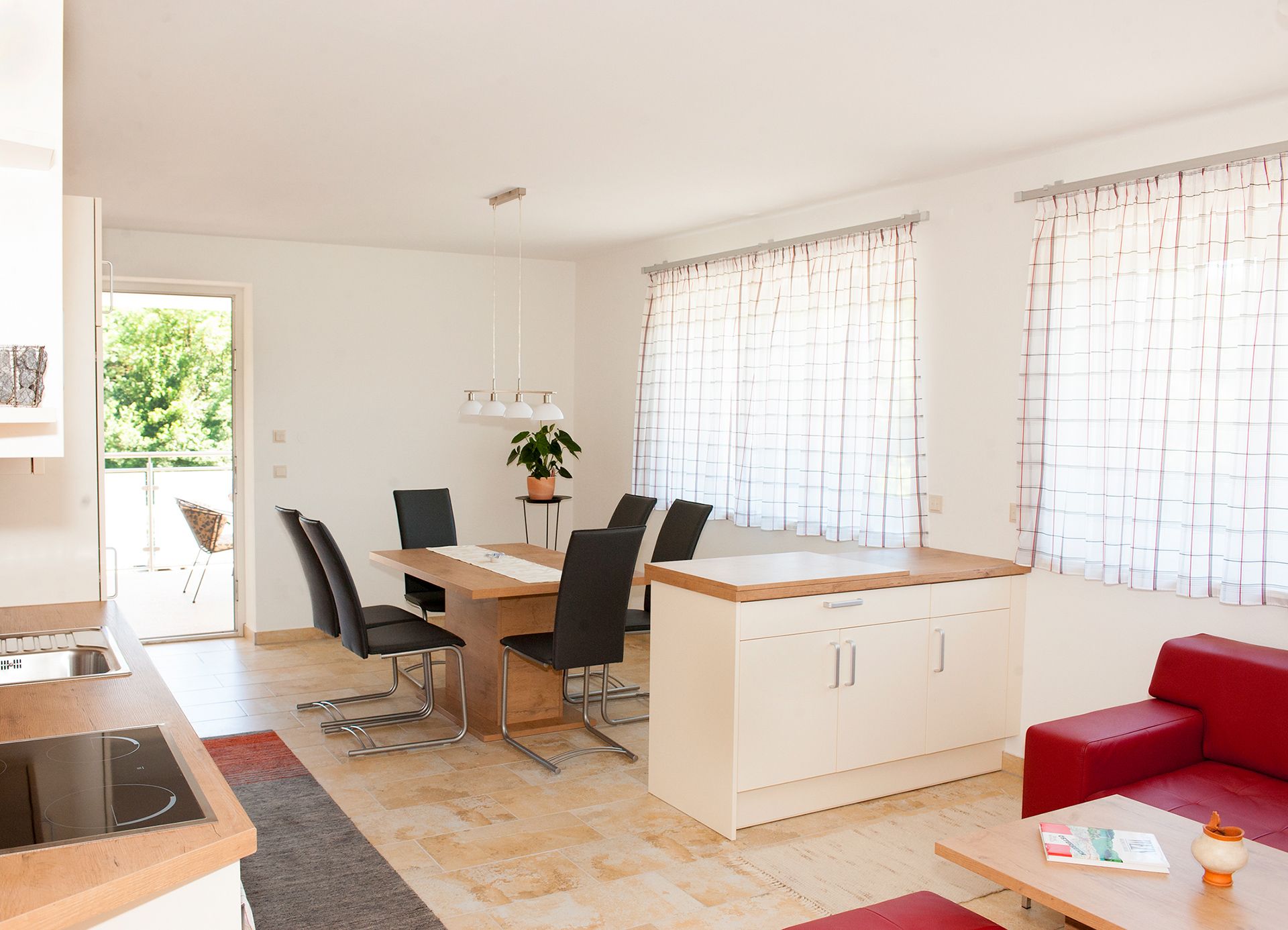 Modern dining area with wooden table, black chairs and large windows with curtains.