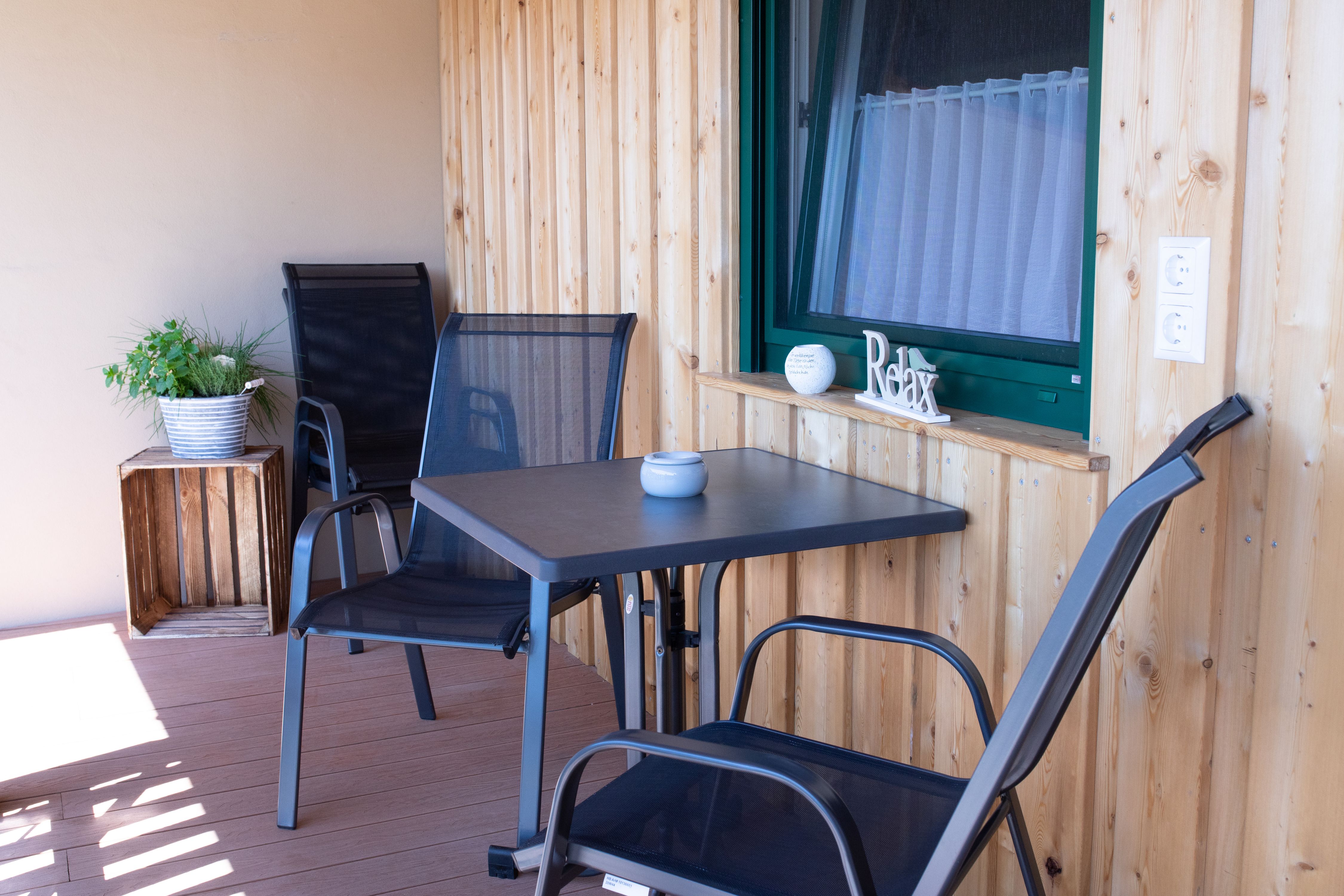 A balcony with wooden walls, two black chairs, a table and a plant in a pot.