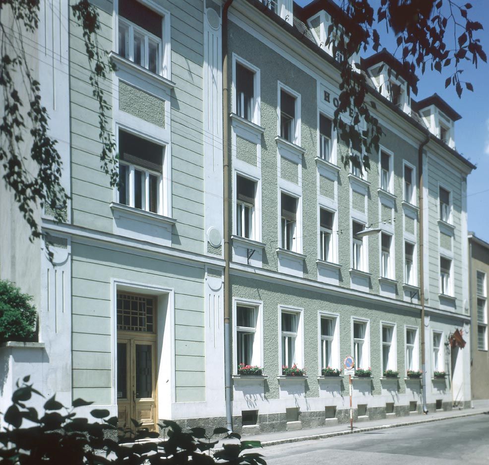 Exterior view of a multi-storey building with a green façade and white window frames.