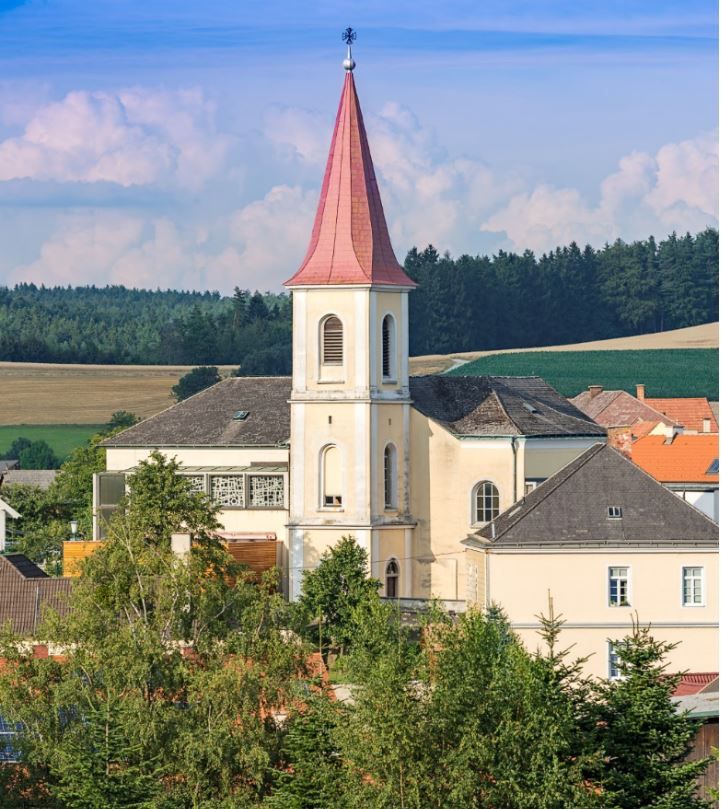 Hochwolkersdorf parish church with red, pointed tower roof and surrounding landscape.