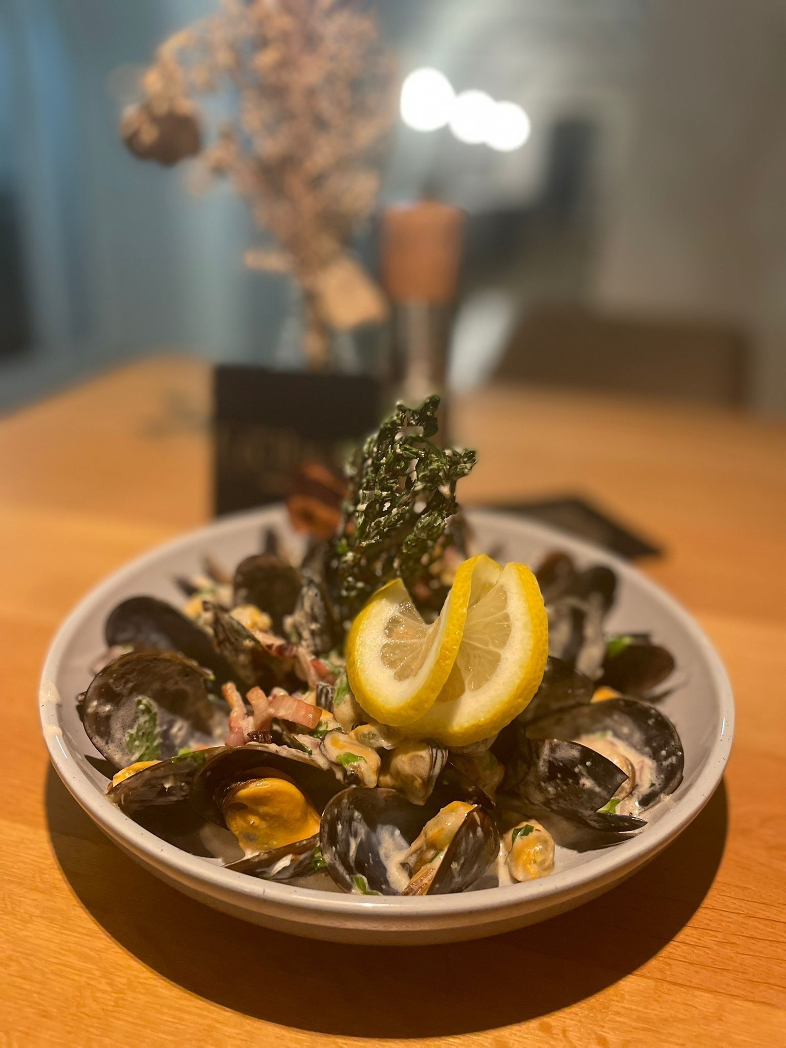 A plate with mussels, cream sauce and lemon slices on a wooden table.